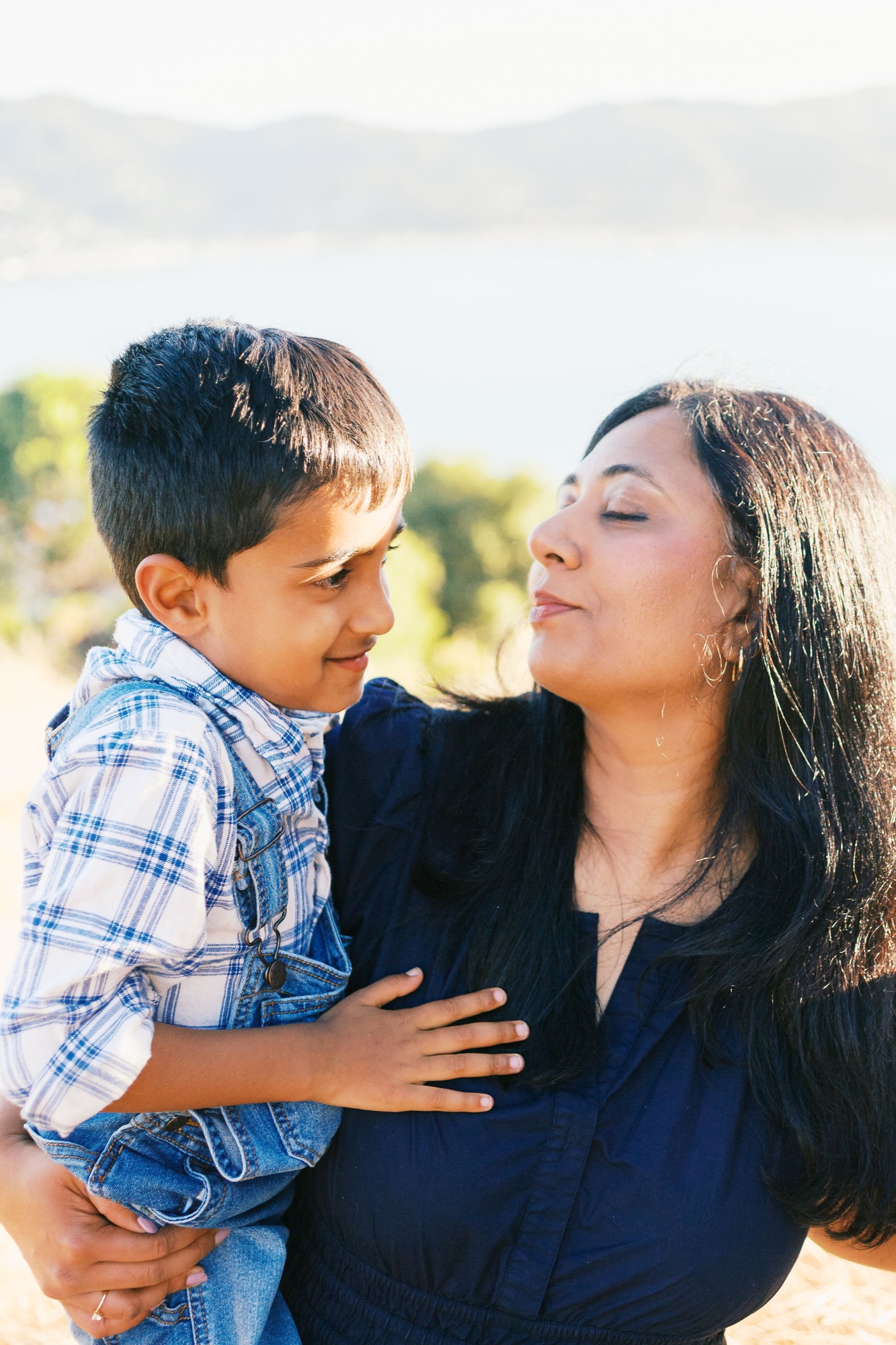 Marin family photographer captures a tender moment between a mother and her young son in golden outdoor light, with the shimmering bay and Marin hills stretching out behind them — authentic family portrait photography in Marin County.
