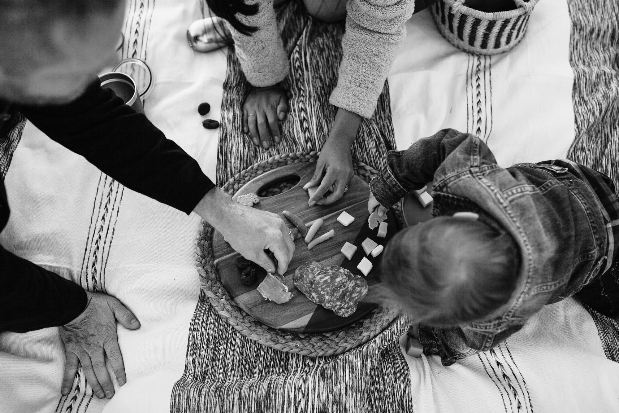 Multiple hands gather around a child holding small objects in a woven basket during an overhead family moment