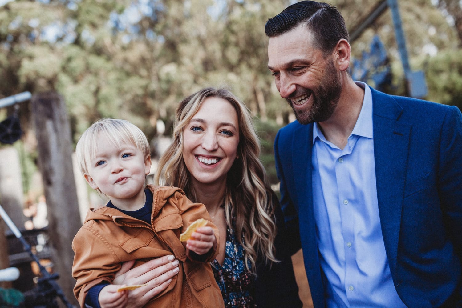 Toddler holding a snack in mom's arms while both parents laugh
