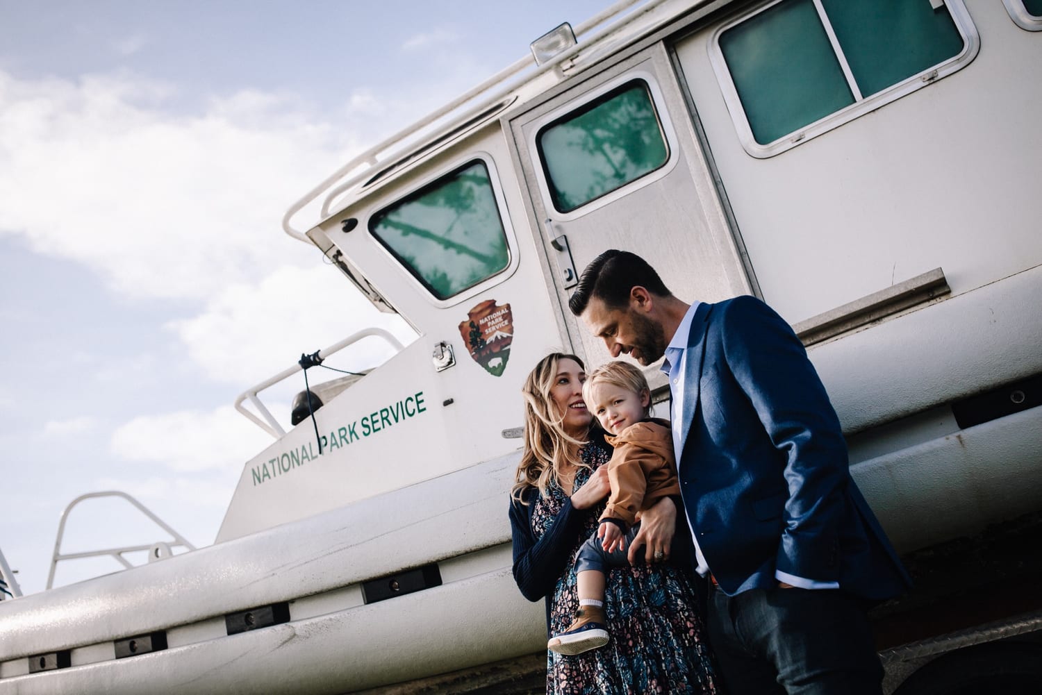 Mom and dad hold their toddler beside a white National Park Service boat