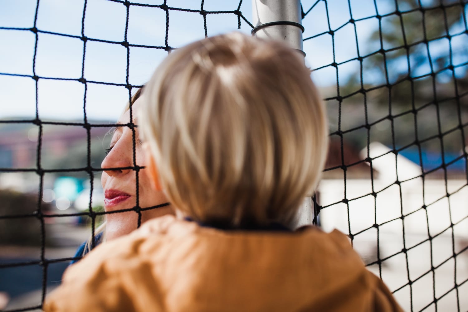 Close-up of mom and toddler peering through playground netting