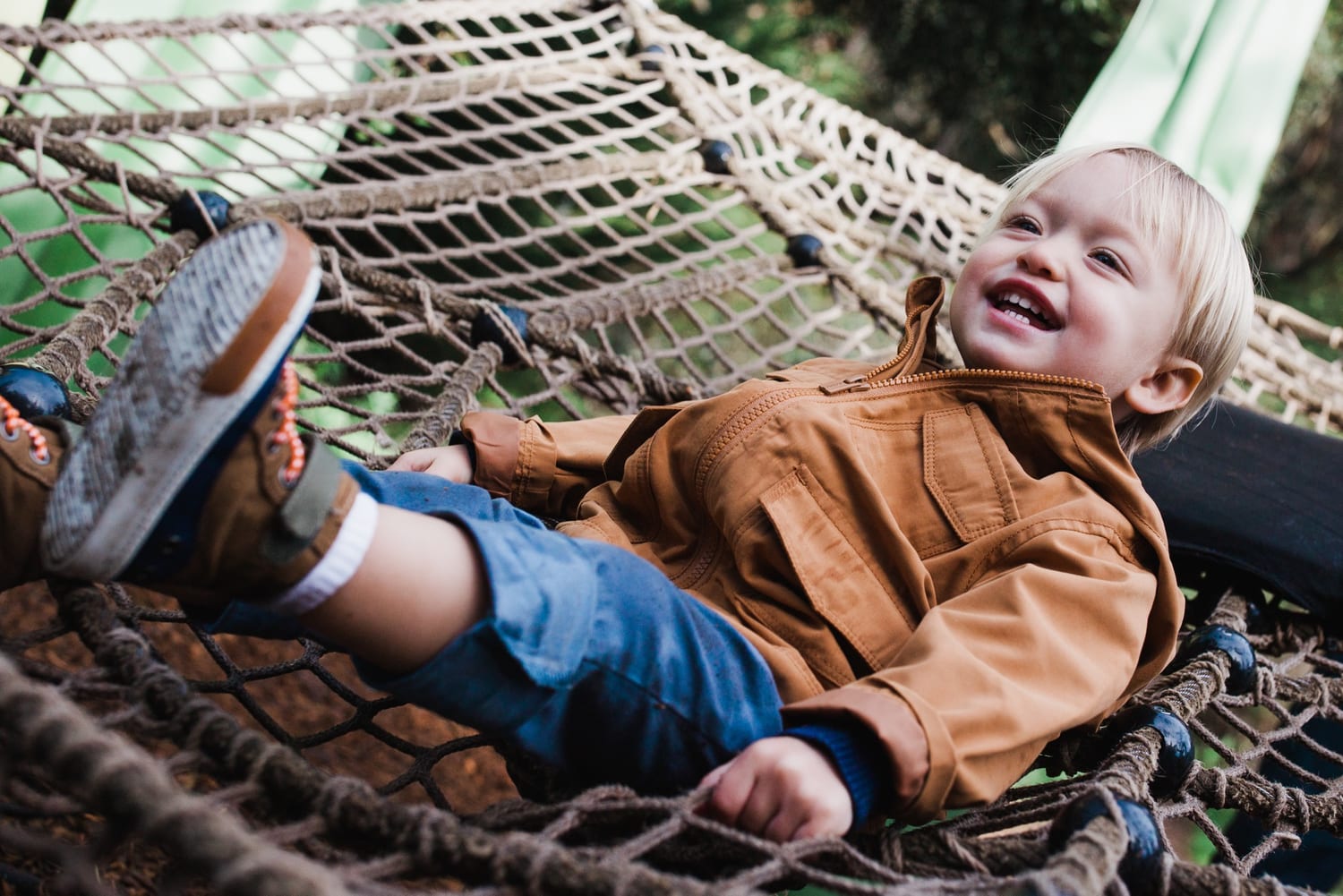 Toddler laughs while lying in a rope climbing net