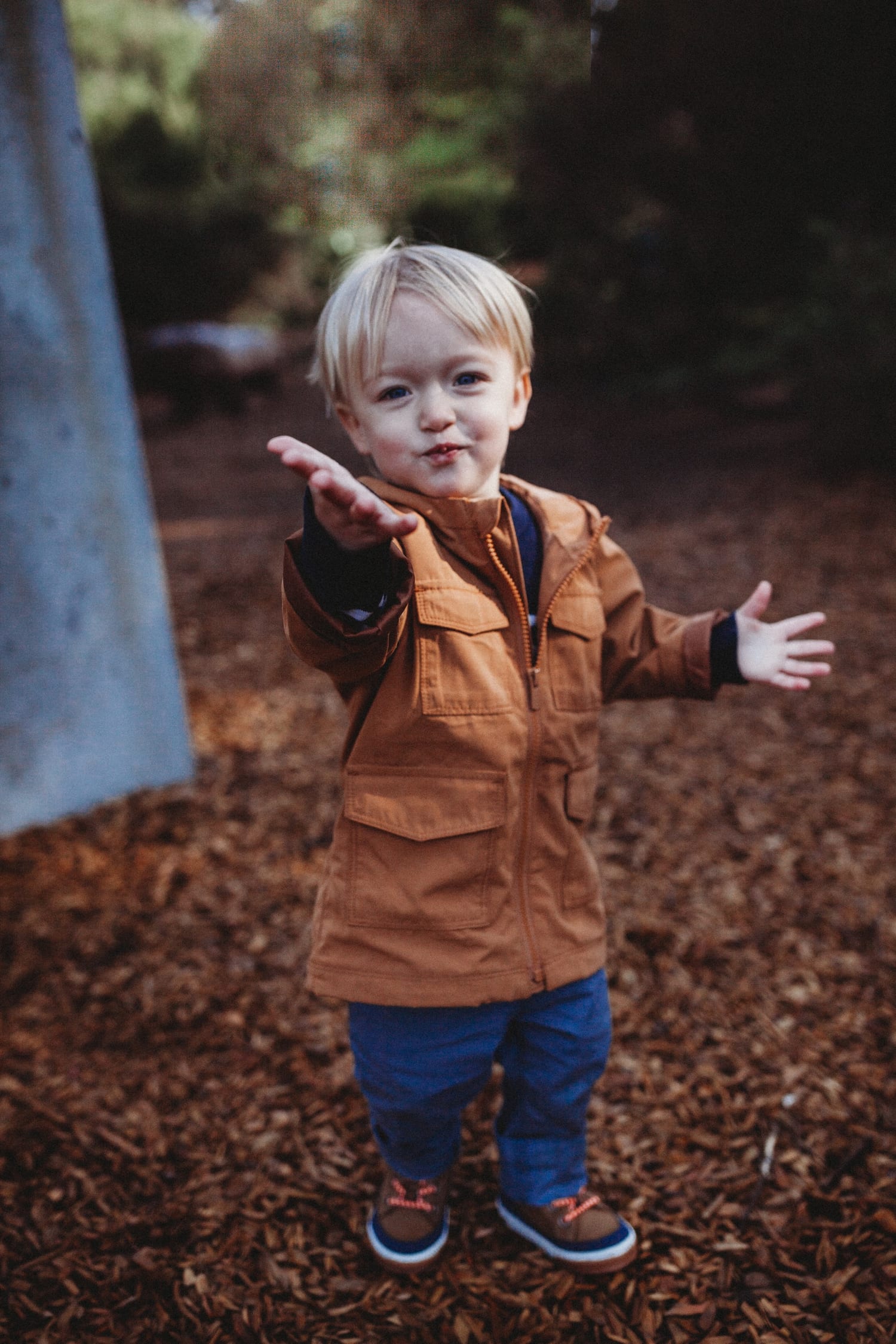 Toddler in a rust jacket reaches both hands out toward the camera