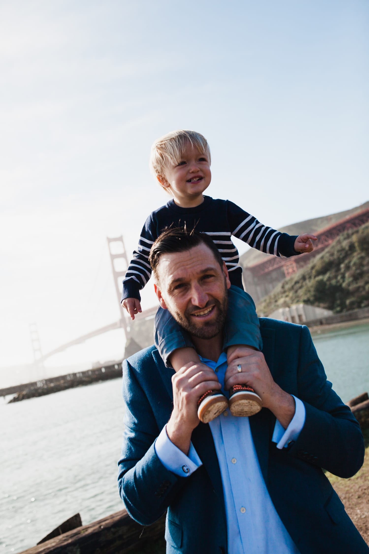 Smiling toddler rides on dad's shoulders with the Golden Gate Bridge behind
