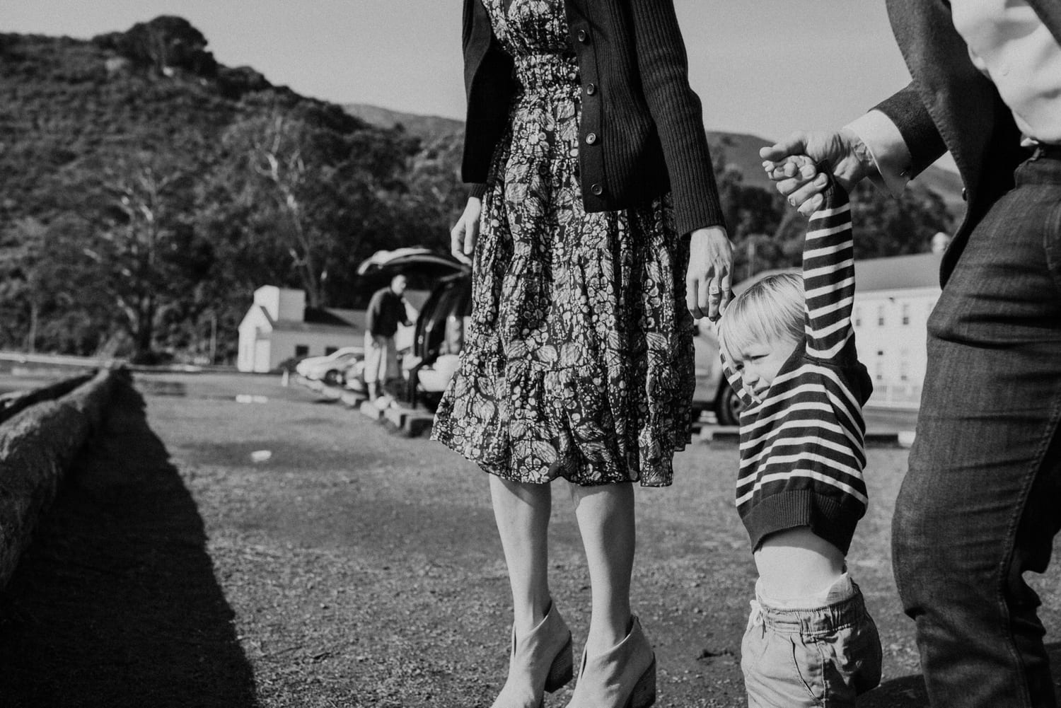 Black and white photo of parents holding their toddler's hands as he swings