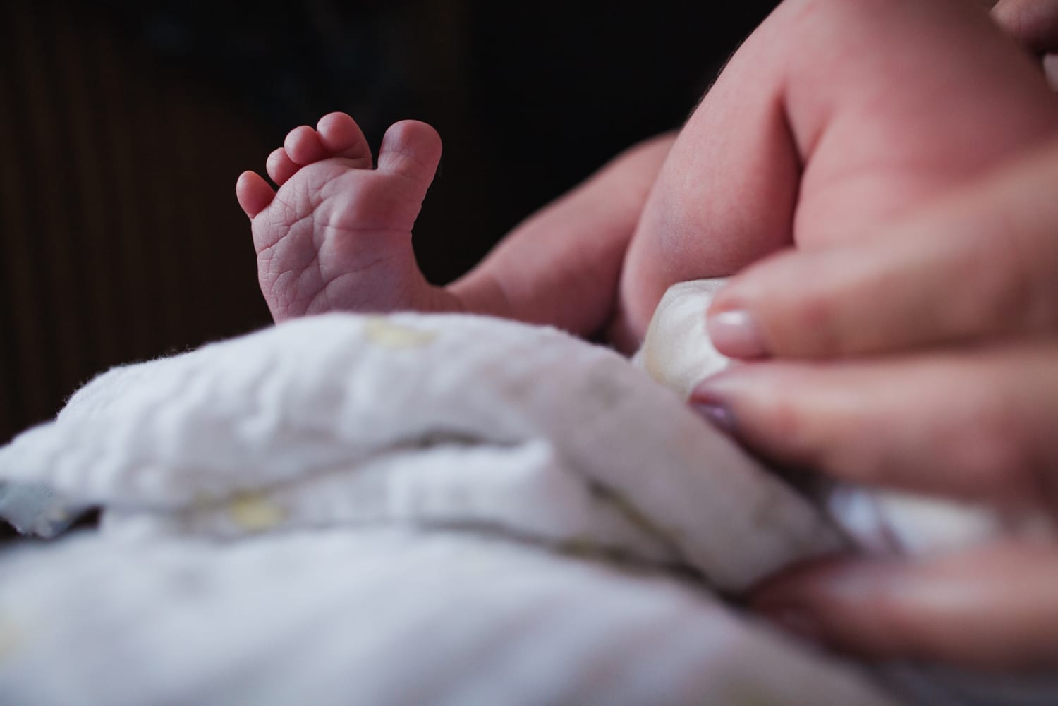 Close-up of tiny newborn feet resting on a white muslin blanket