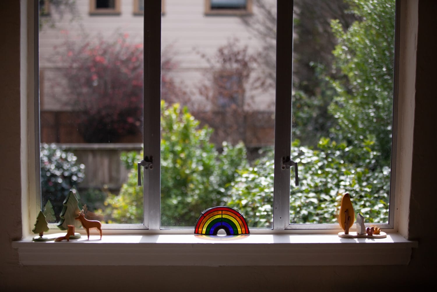 Nursery windowsill with wooden animal toys and a stained glass rainbow