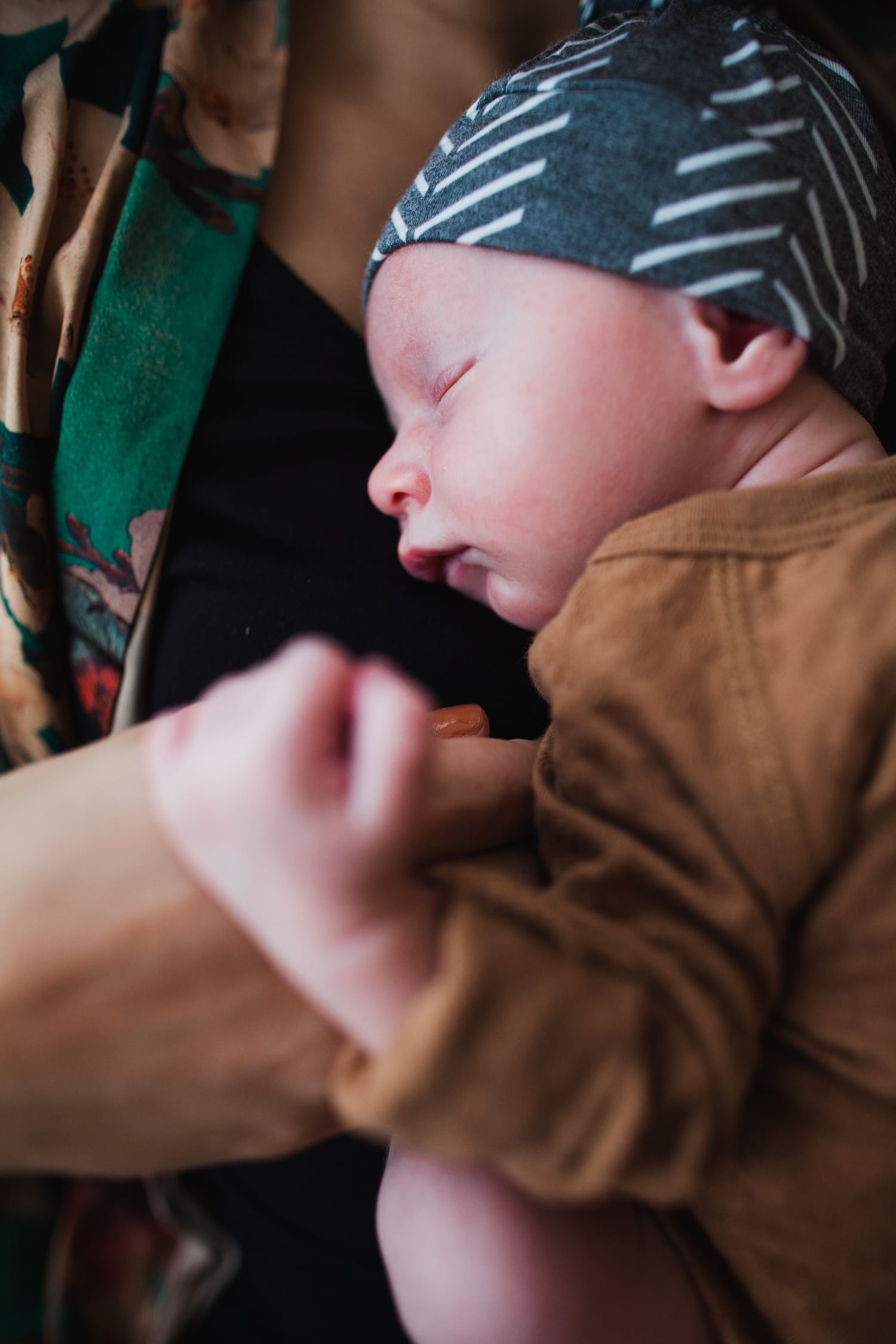 Sleeping newborn in a brown onesie and knotted hat curled on mom's chest