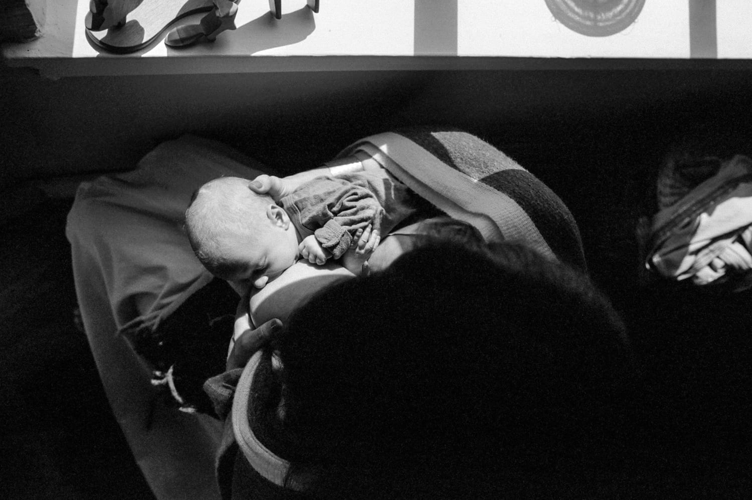 Black and white overhead view of mom breastfeeding her newborn in window light