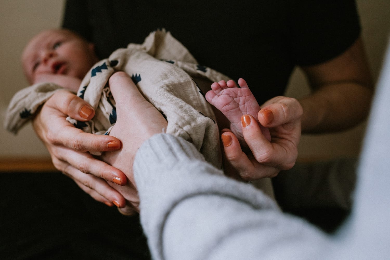 Parents' hands cradle their newborn, one tiny foot in the foreground