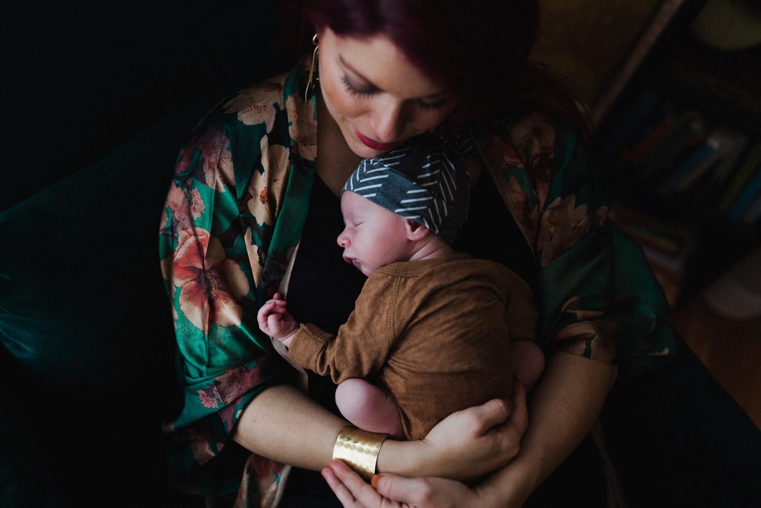 Mom bows her head over her sleeping newborn in a brown onesie