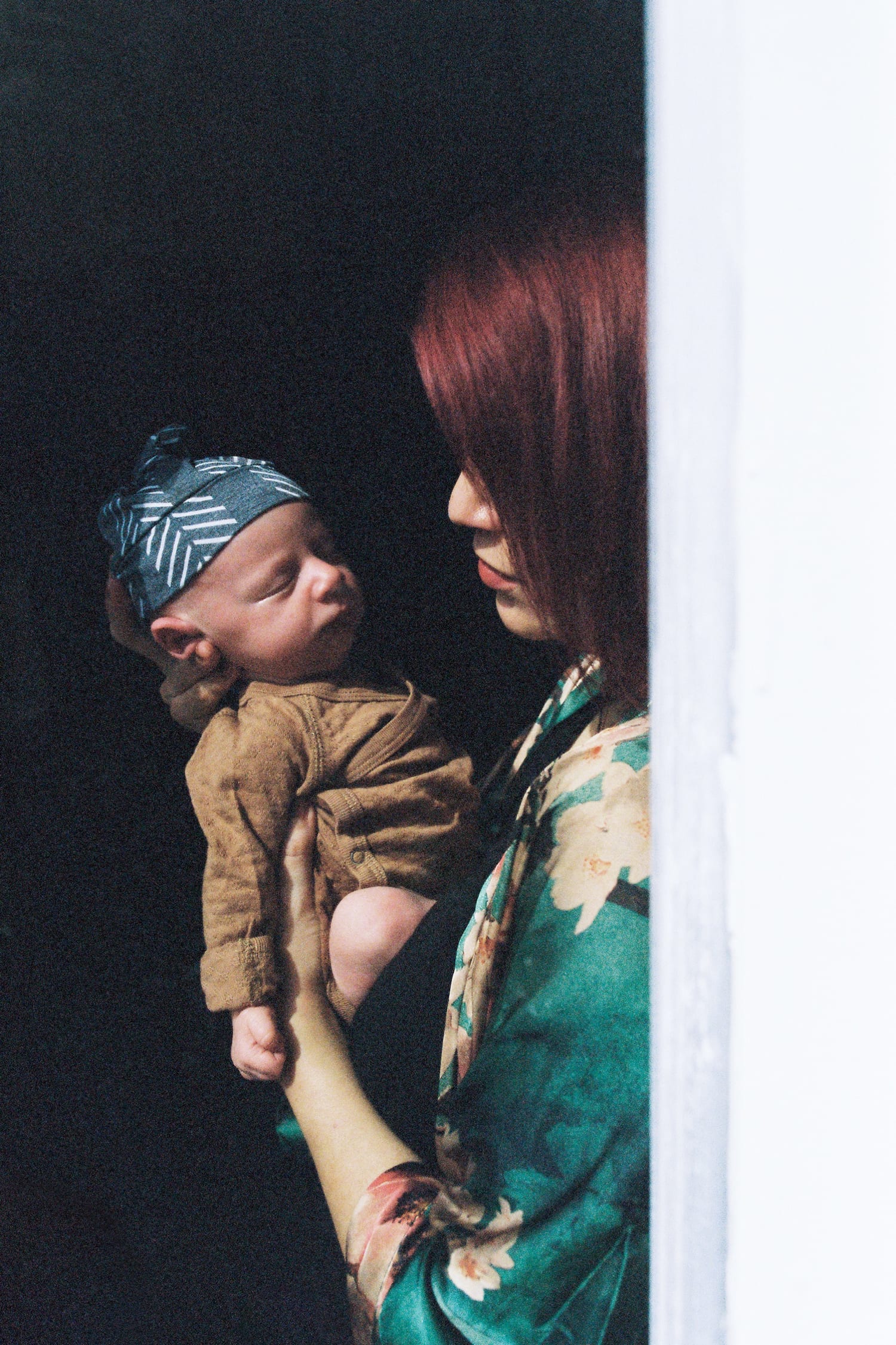 Mom holds her sleeping newborn in a shaft of sunlight by the doorway