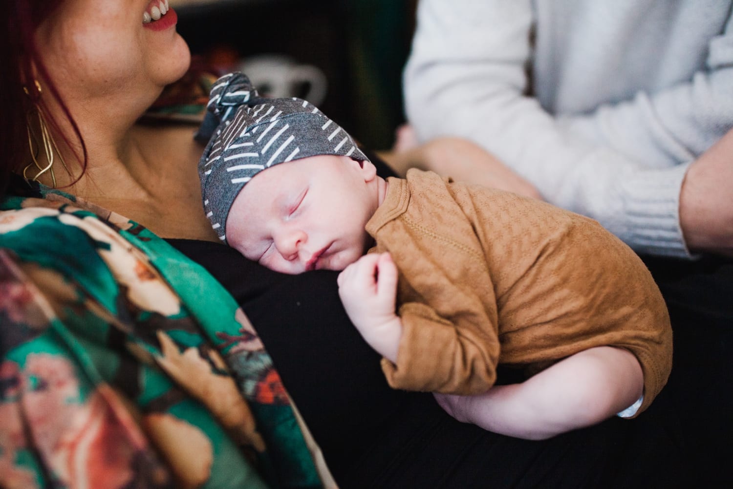 Newborn in a knotted hat sleeps on mom's chest while she smiles