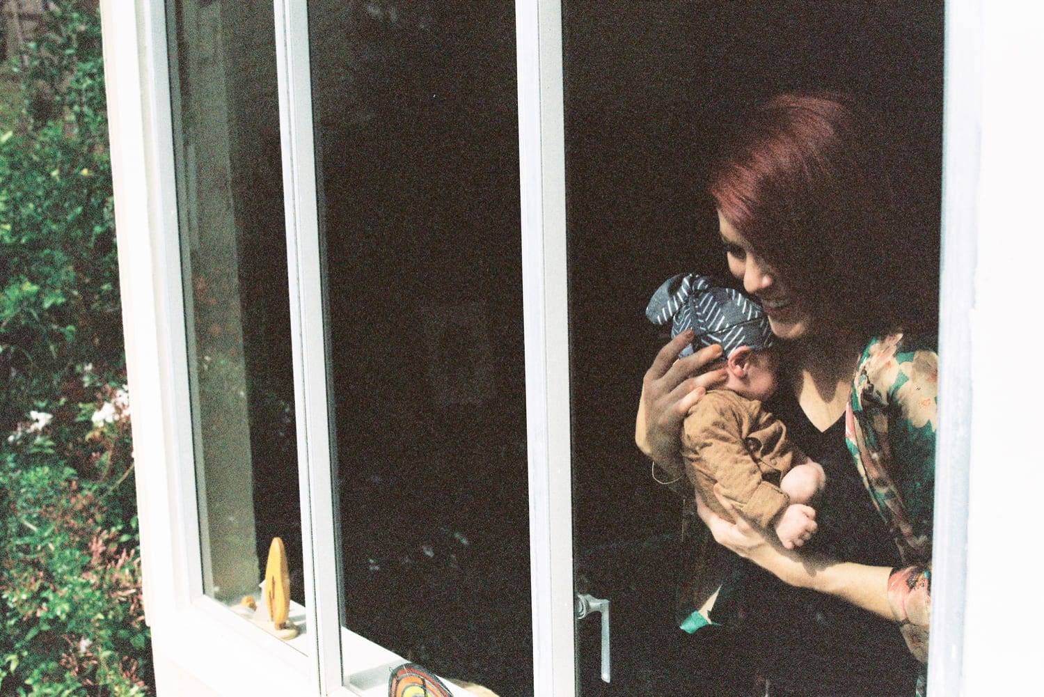 Seen through the window, mom smiles down at her newborn in her arms