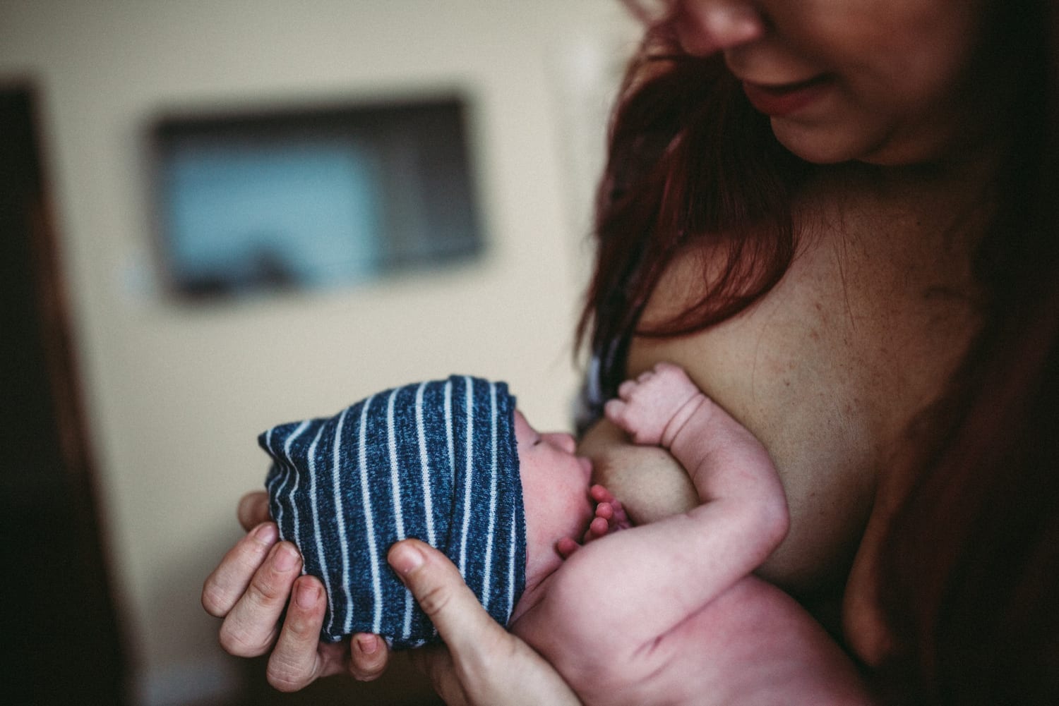 Mom breastfeeds her newborn, baby wrapped in a striped blue swaddle