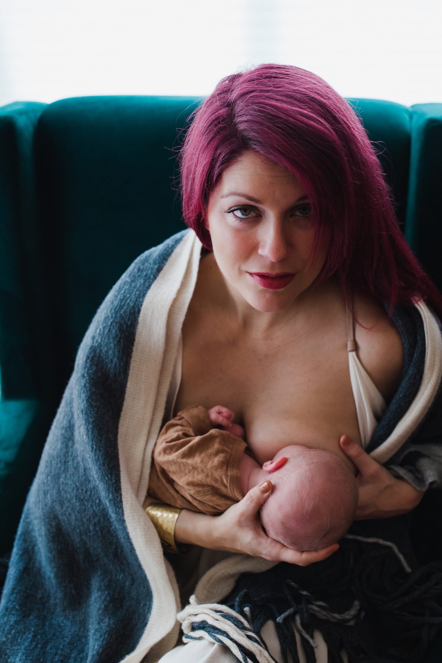 Mom glances up while nursing her newborn under a cozy blanket