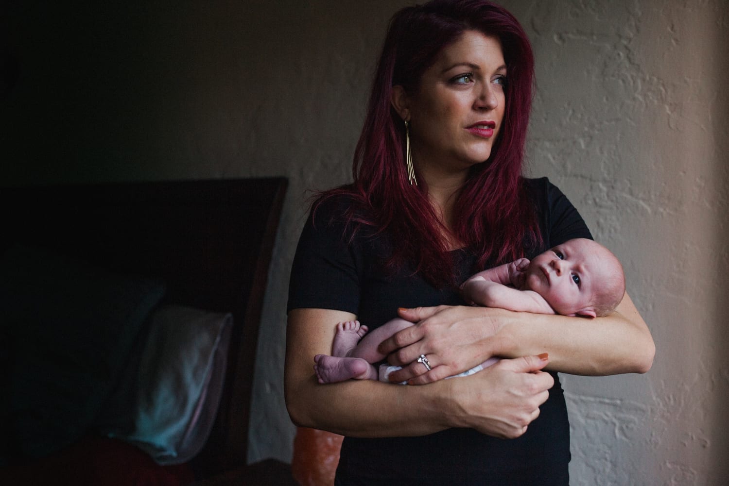Mom looks toward the window light while cradling her newborn in her arms
