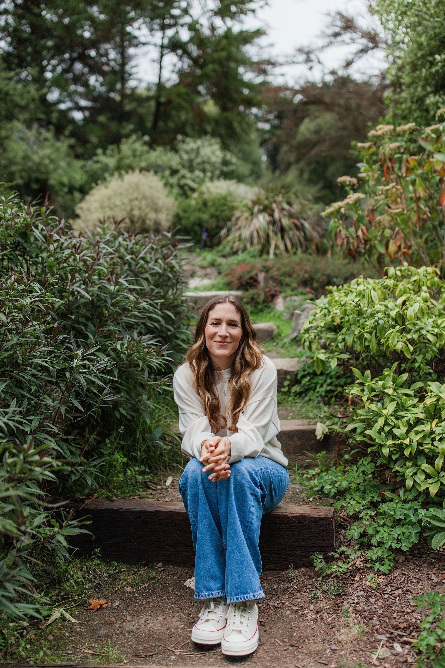 Full-body lifestyle headshot sitting on a garden bench surrounded by greenery — Marin County