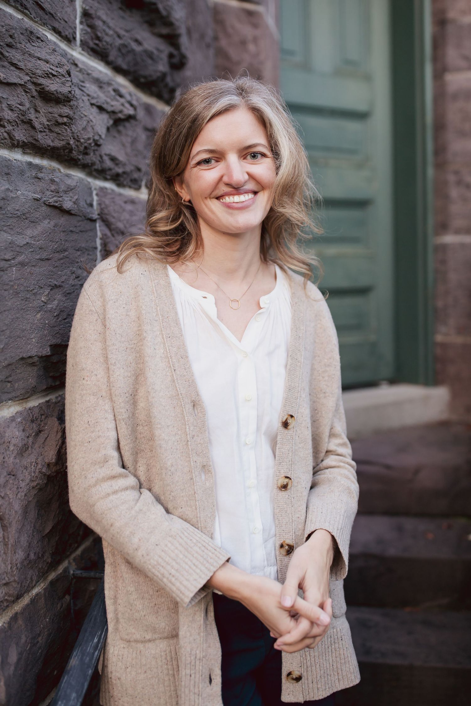 Casual headshot against a stone wall in a beige cardigan — on-location portrait