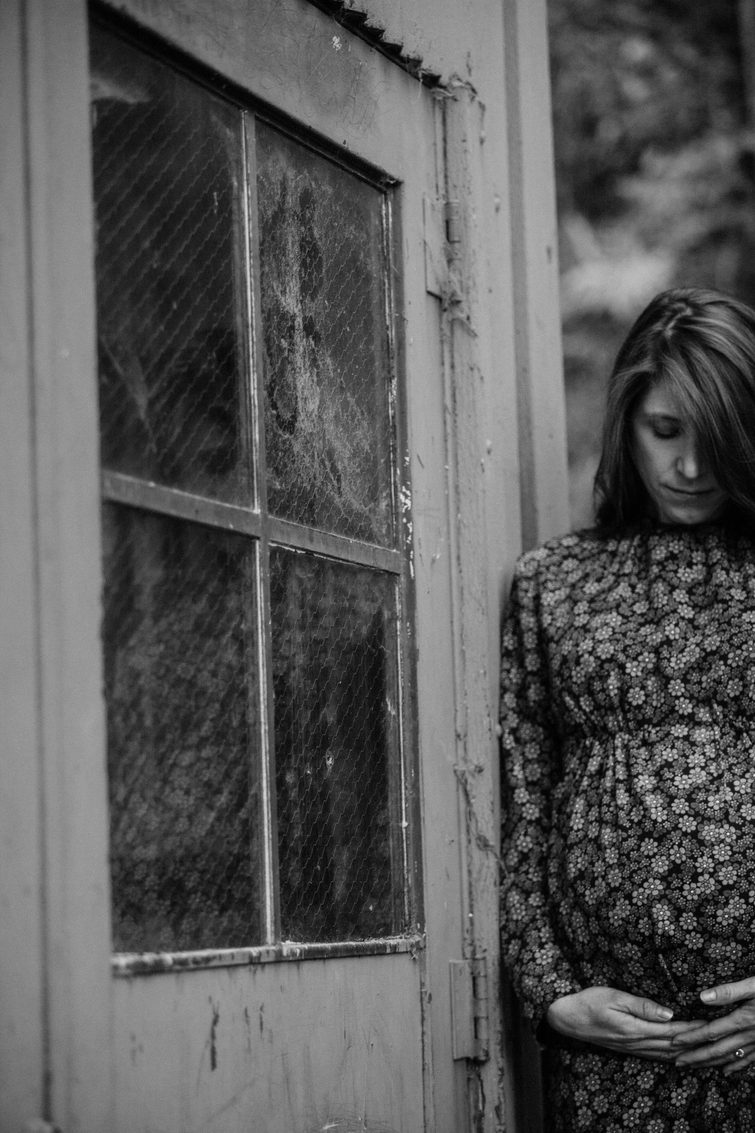 Moody black and white maternity portrait next to a weathered door