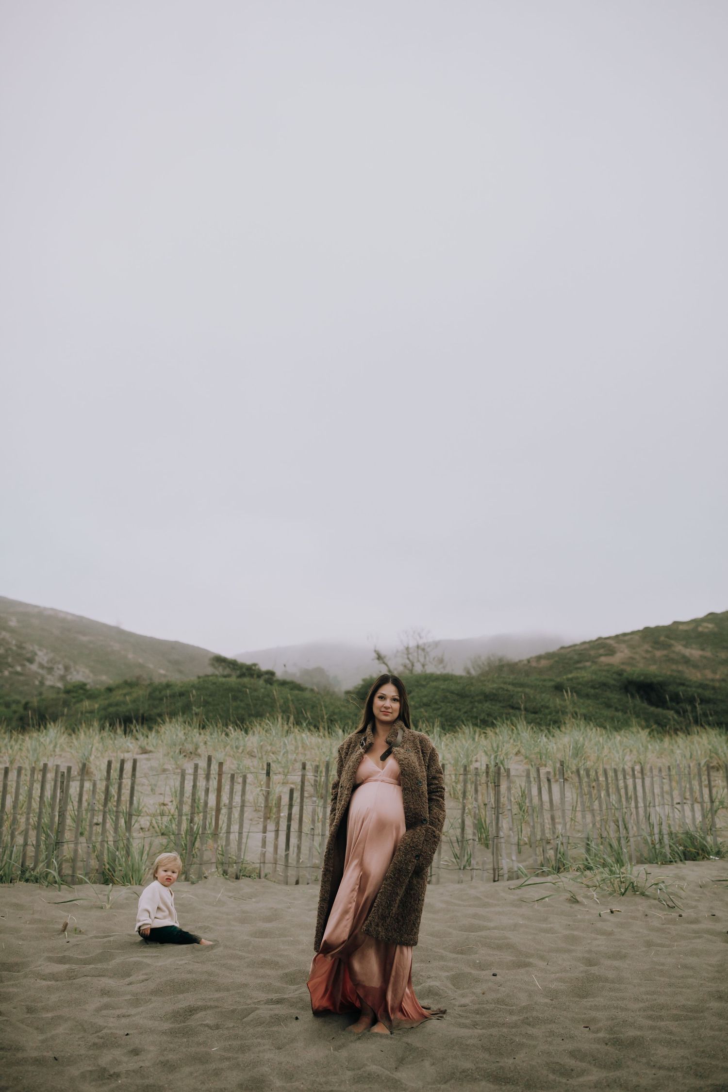 Pregnant woman in pink dress at the beach with sand dunes and a toddler — maternity session in Marin County