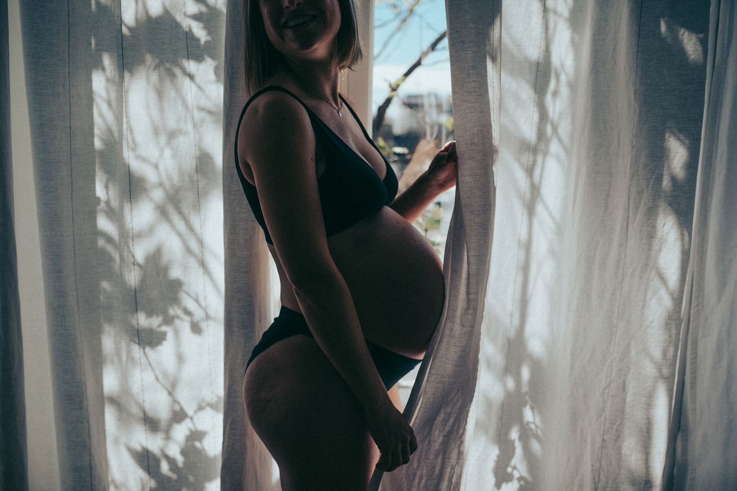 Artistic silhouette of a pregnant woman standing by a window — in-home maternity session in Marin County