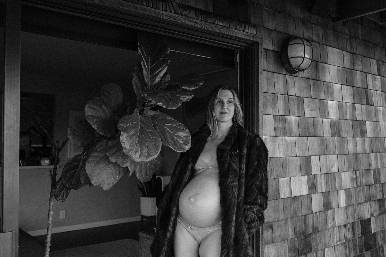 Pregnant woman in a fur coat standing outside a cedar-shingled home — maternity photography in Marin County