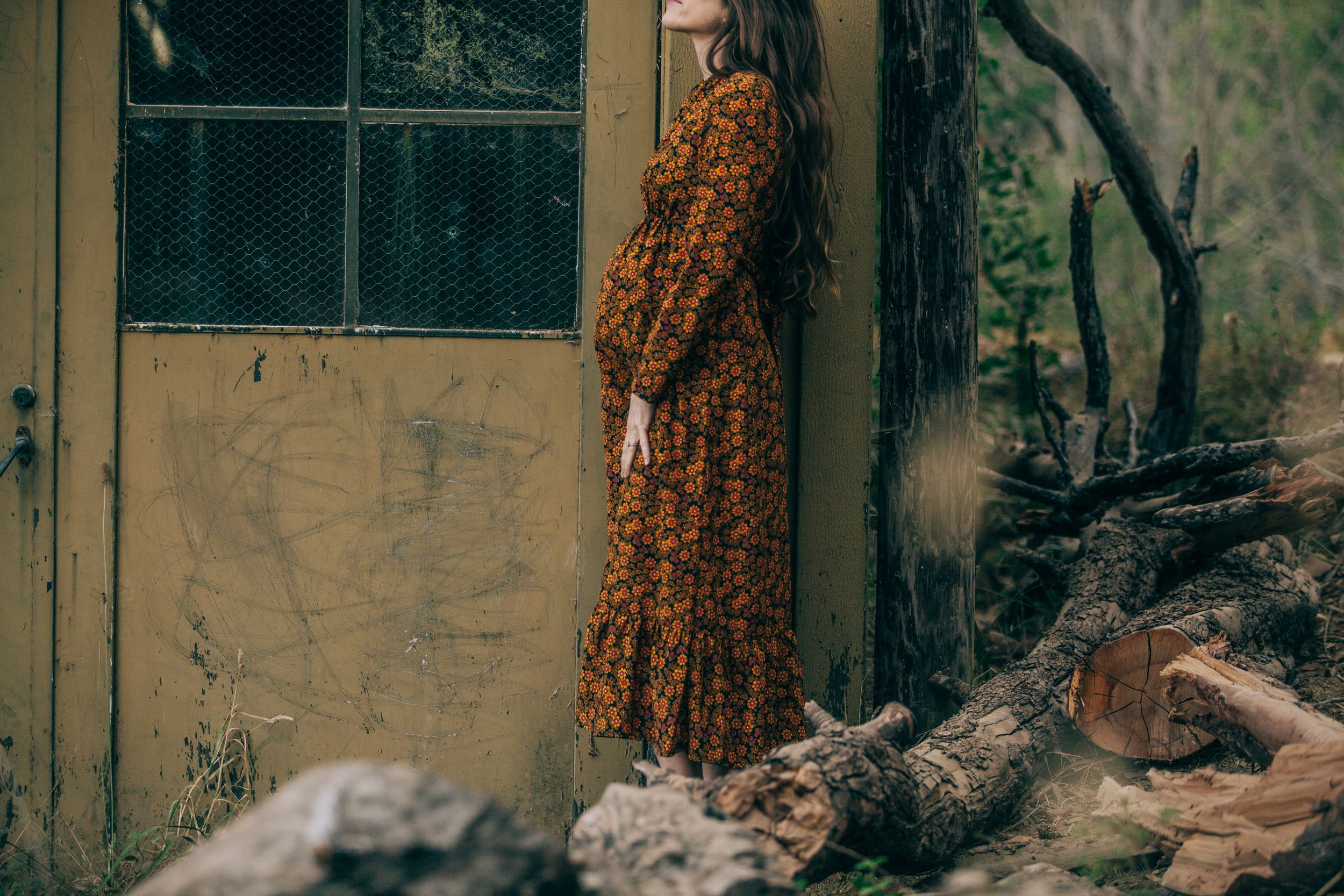 Person in floral dress standing against a weathered yellow wall — maternity portrait in Marin County