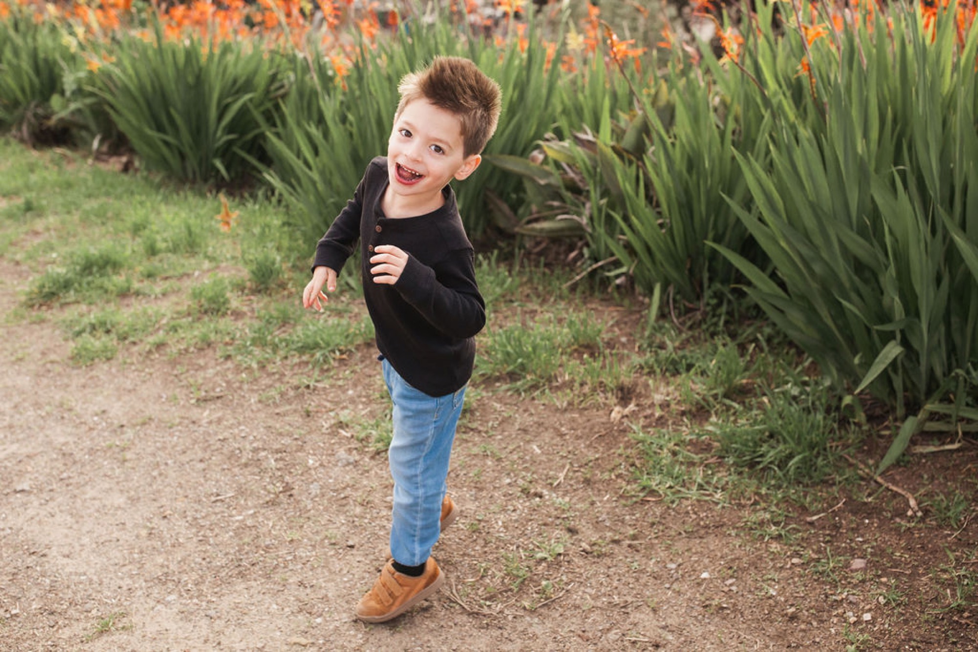 Young child running joyfully on a dirt path with orange wildflowers and green foliage blooming behind