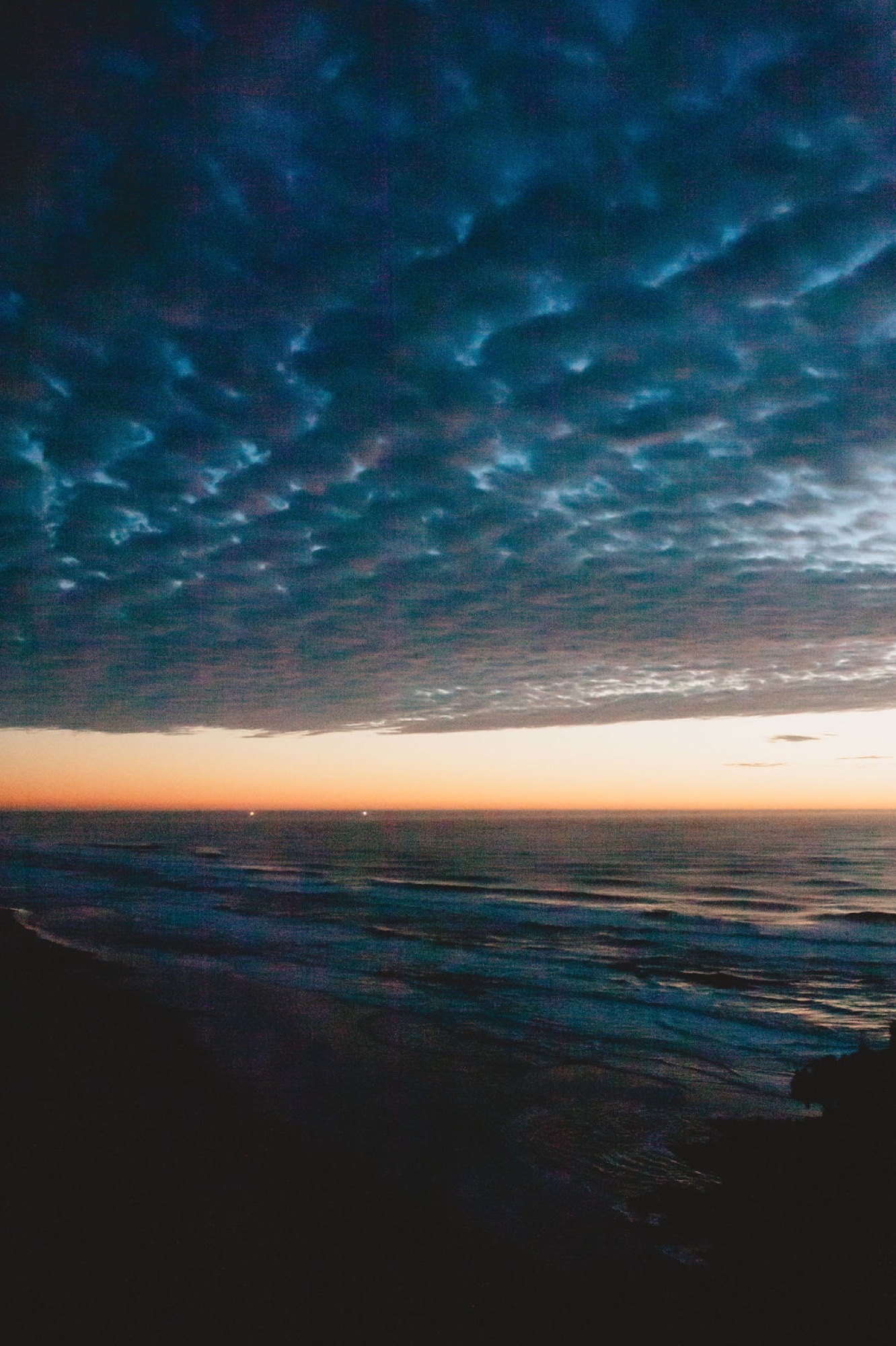 Dramatic twilight sky with deep teal clouds frames a distant coastline and darkened shoreline at dusk