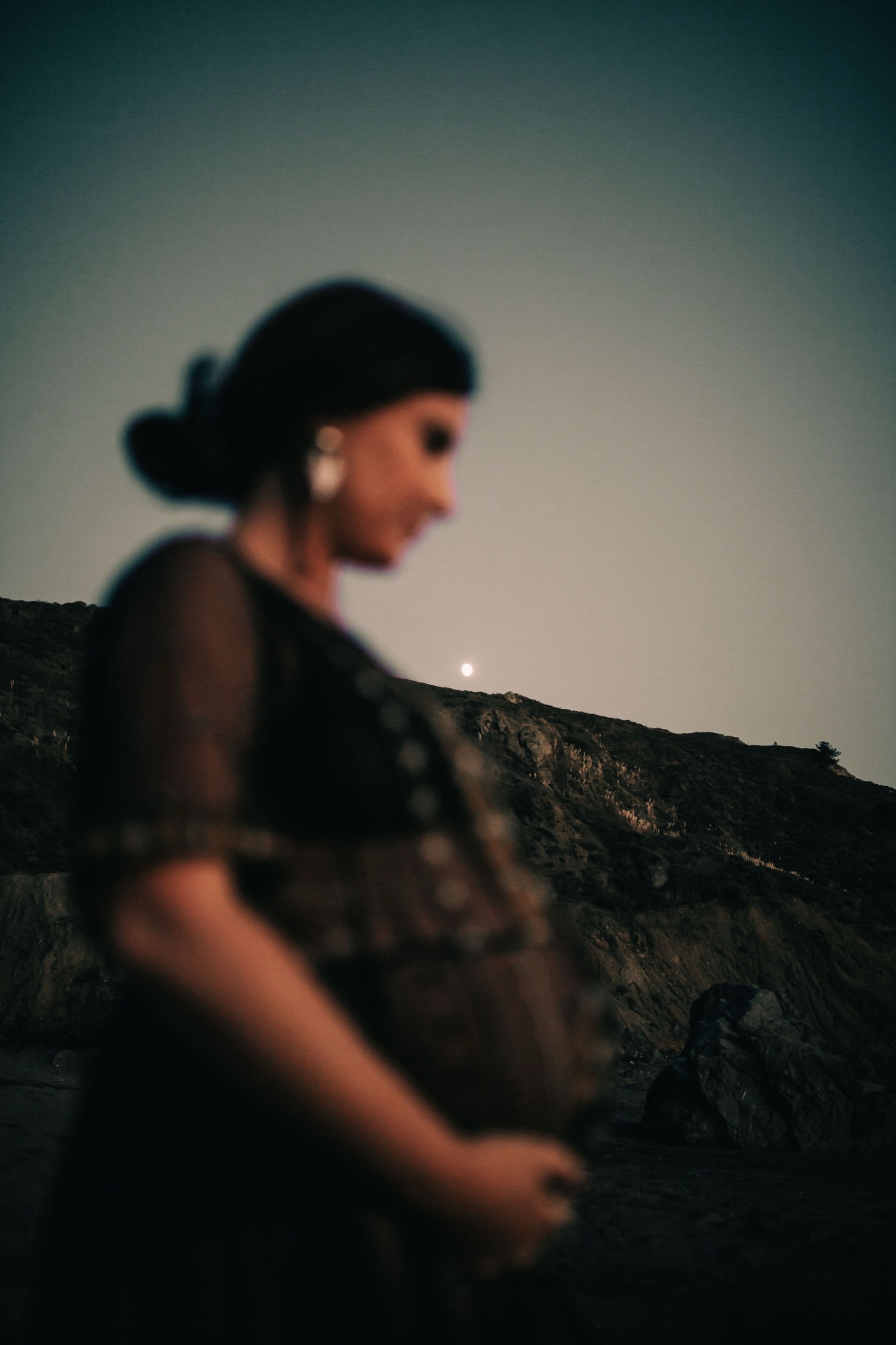 A woman in profile gazes toward the horizon from a rocky hilltop at dusk, silhouetted against the fading light