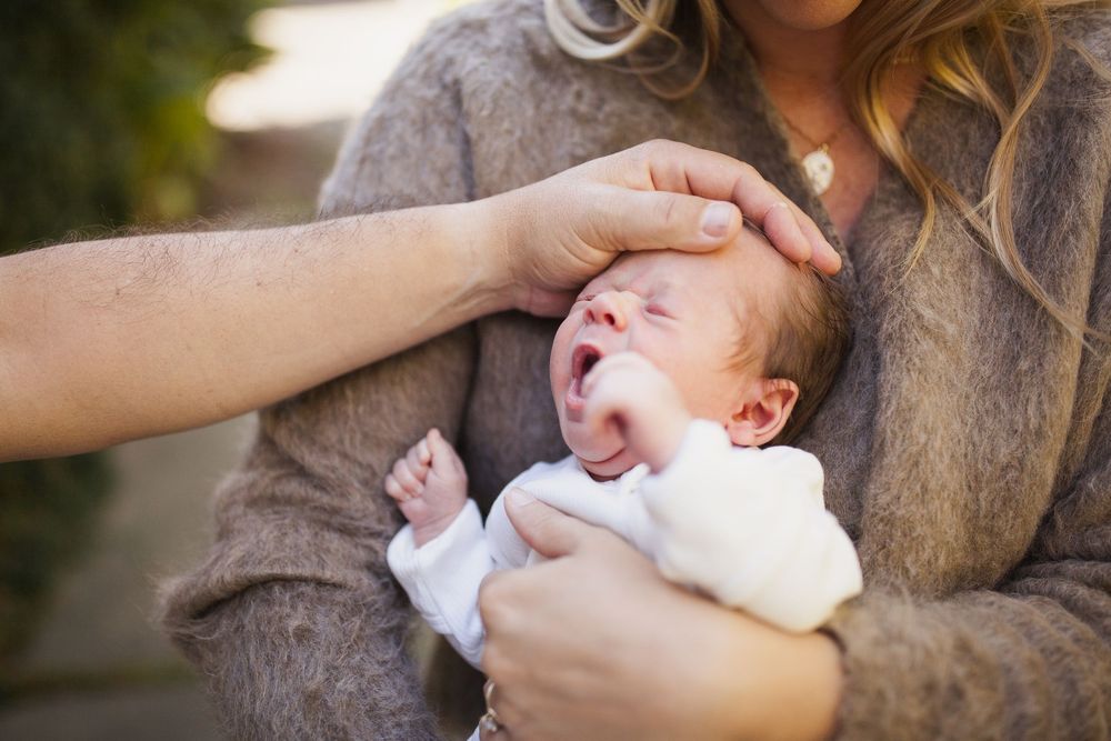 Parent gently holding a yawning newborn outdoors in warm golden light — San Anselmo Newborn Photographer