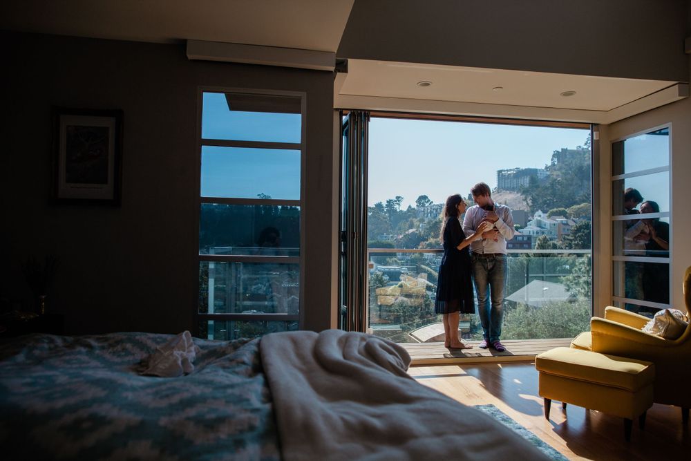 Parents silhouetted in a sunlit doorway with city view, holding their newborn — in-home lifestyle session