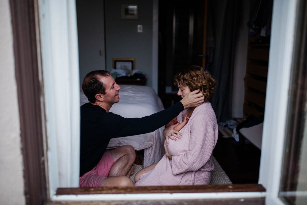 Couple with newborn photographed through a window frame — lifestyle newborn photography in Marin County — San Anselmo Newborn Photographer