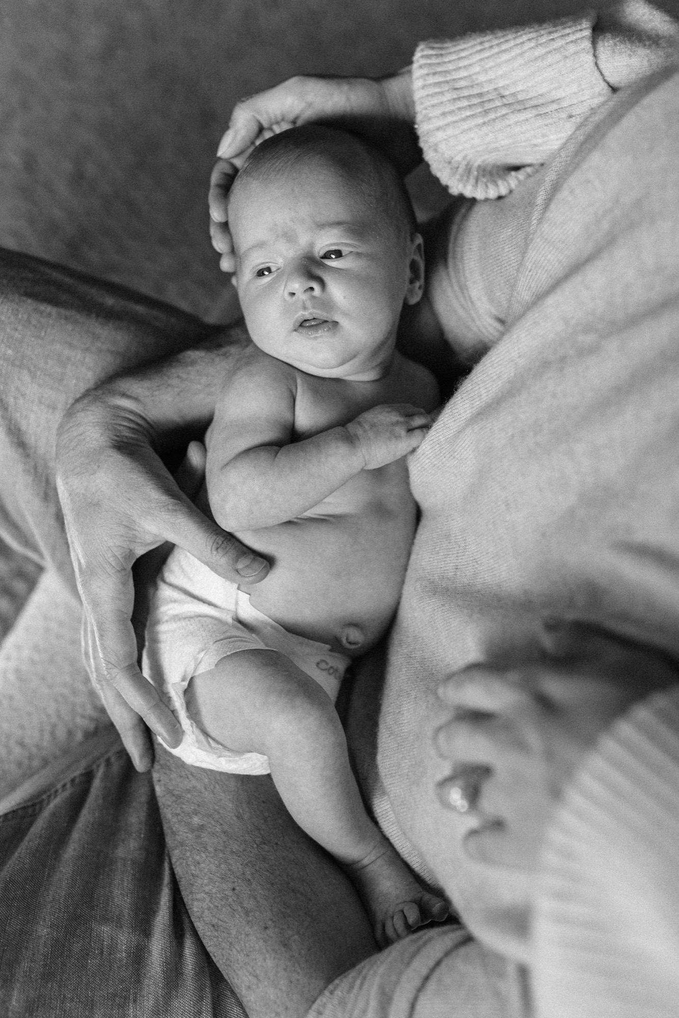 That wide-eyed, searching gaze — a brand new Marin County baby looking up toward her parent as if discovering the world for the very first time — is the kind of fleeting moment that disappears in a matter of days. Cradled in a gentle cocoon of arms and soft natural light, this little one's curious expression tells the whole story of those tender early hours at home.