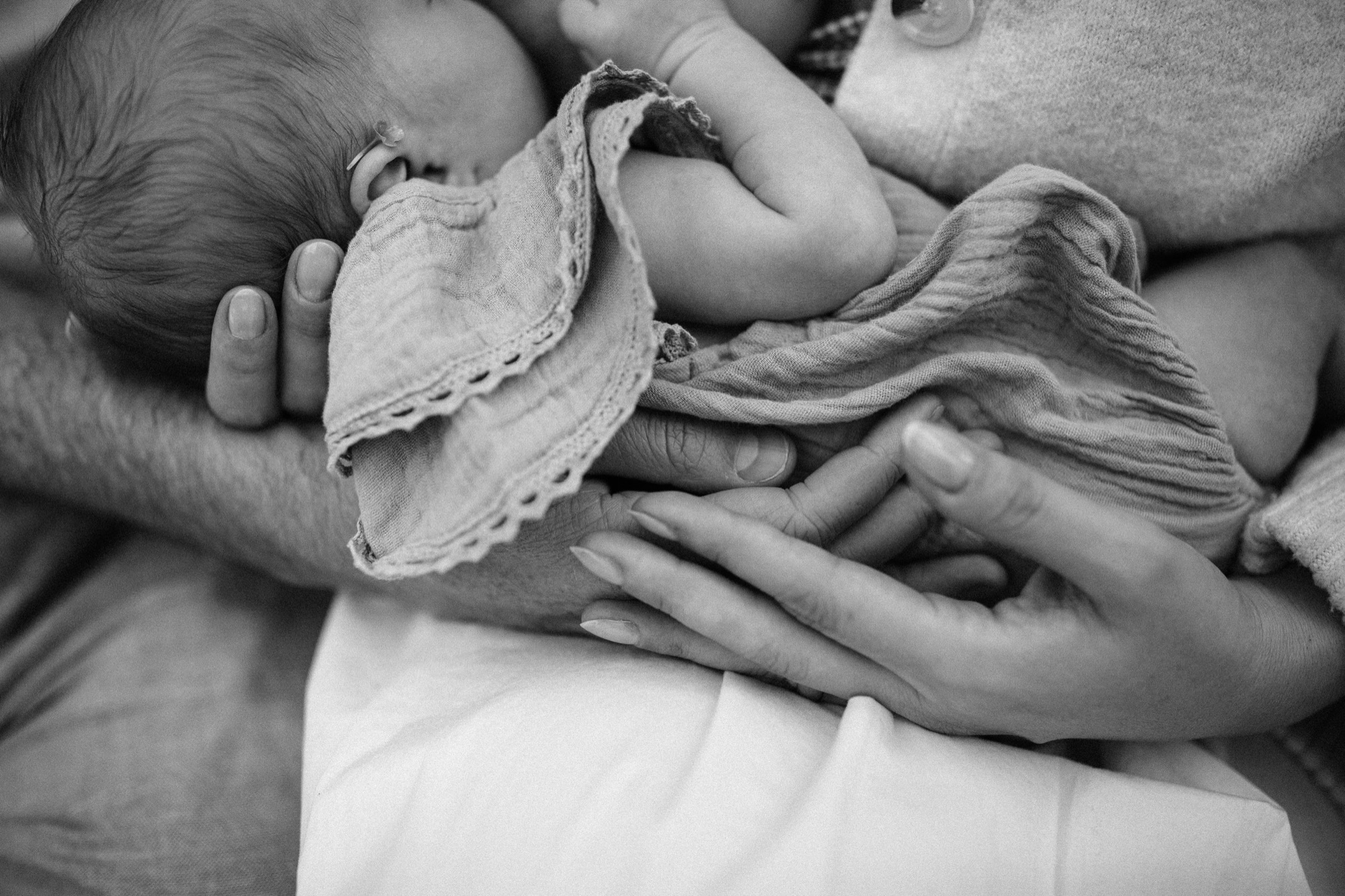Two sets of hands (strong and delicate) wrapped around a sage green swaddled newborn in the soft natural light of a Marin County home