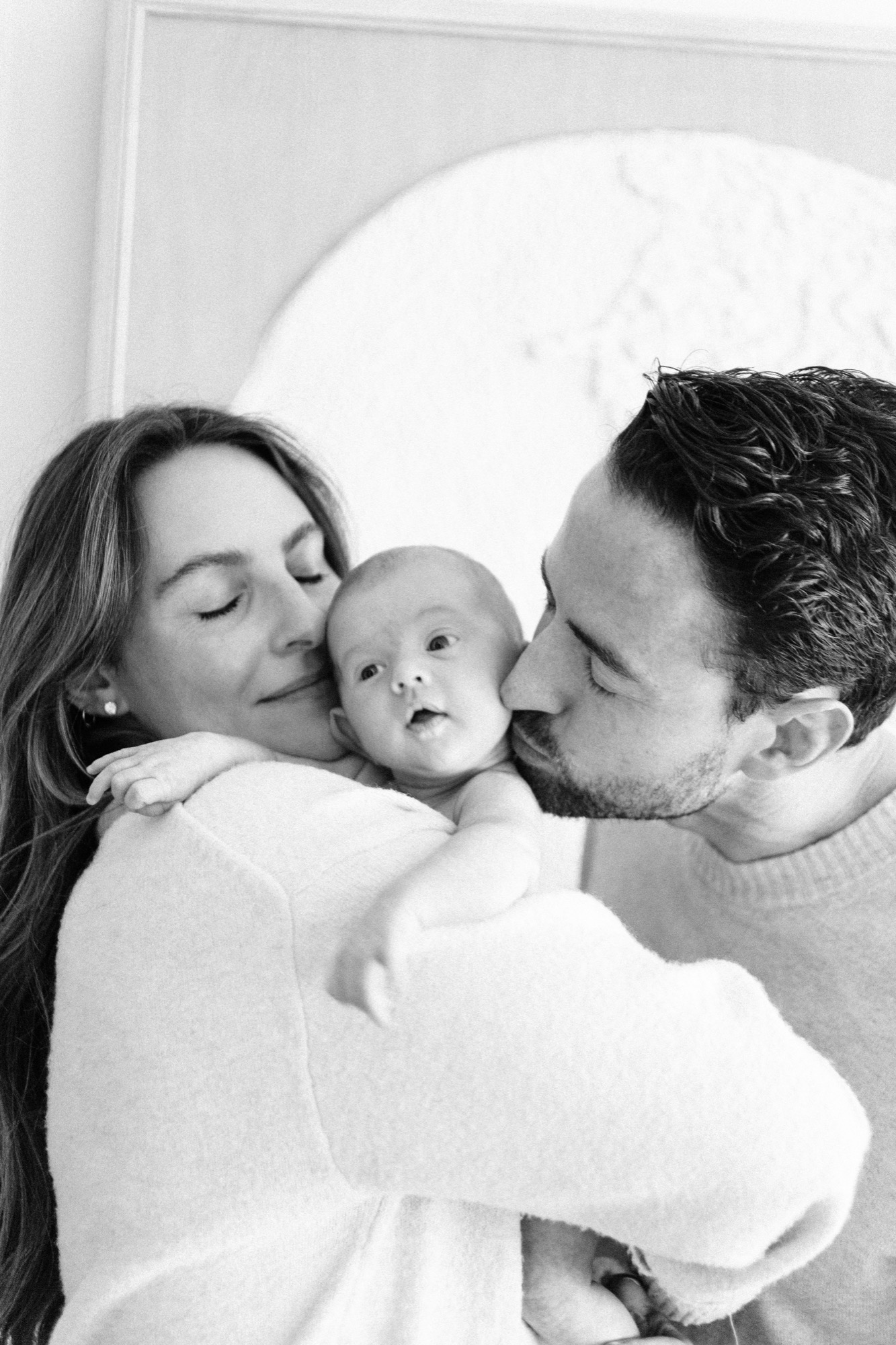 Both parents kiss their newborn's cheeks while she gazes up between them