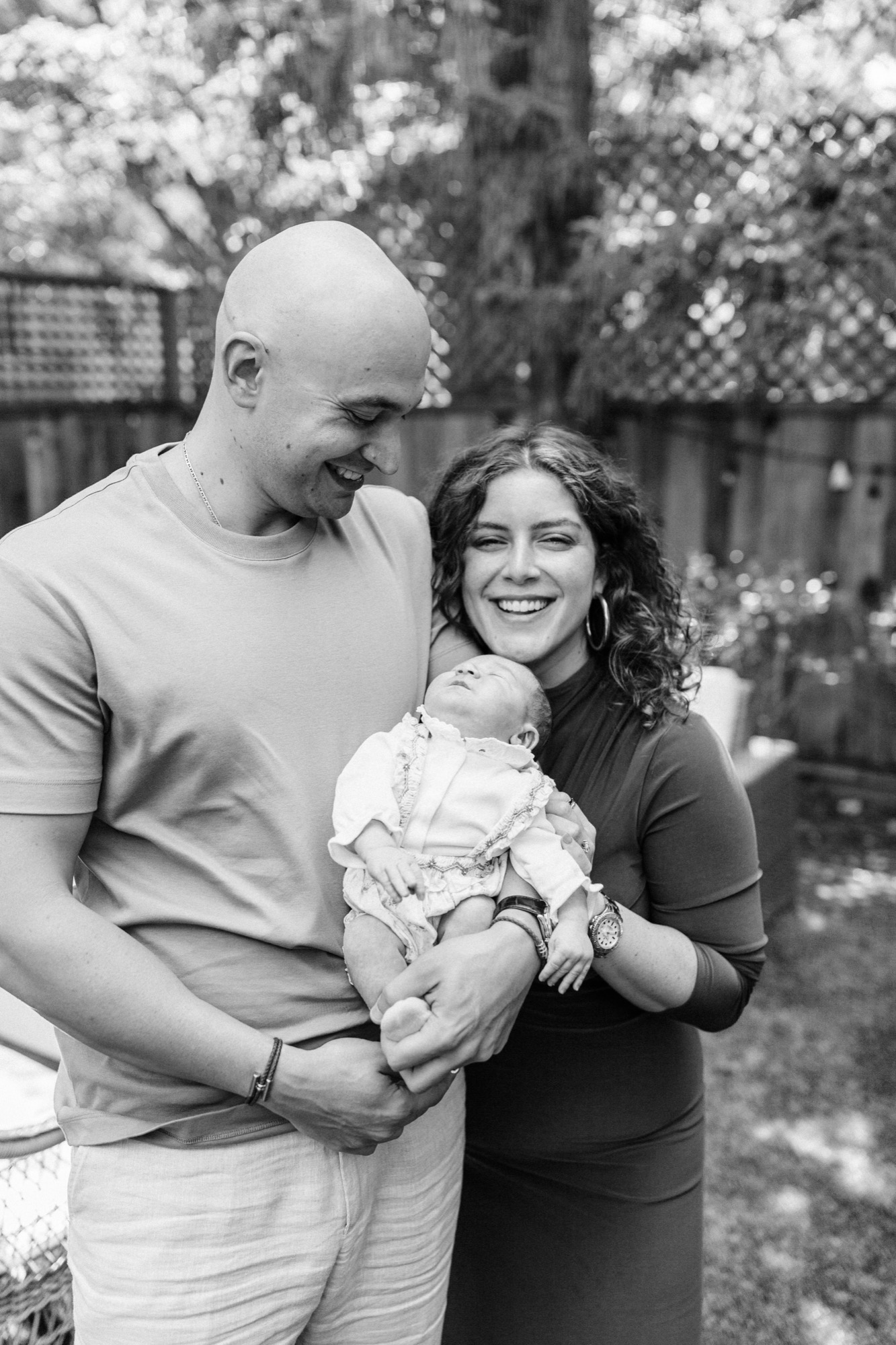 Marin newborn photographer captures a joyful family portrait of parents cradling their two-week-old daughter in soft outdoor light at their Palo Alto home — Bay Area lifestyle newborn photography.