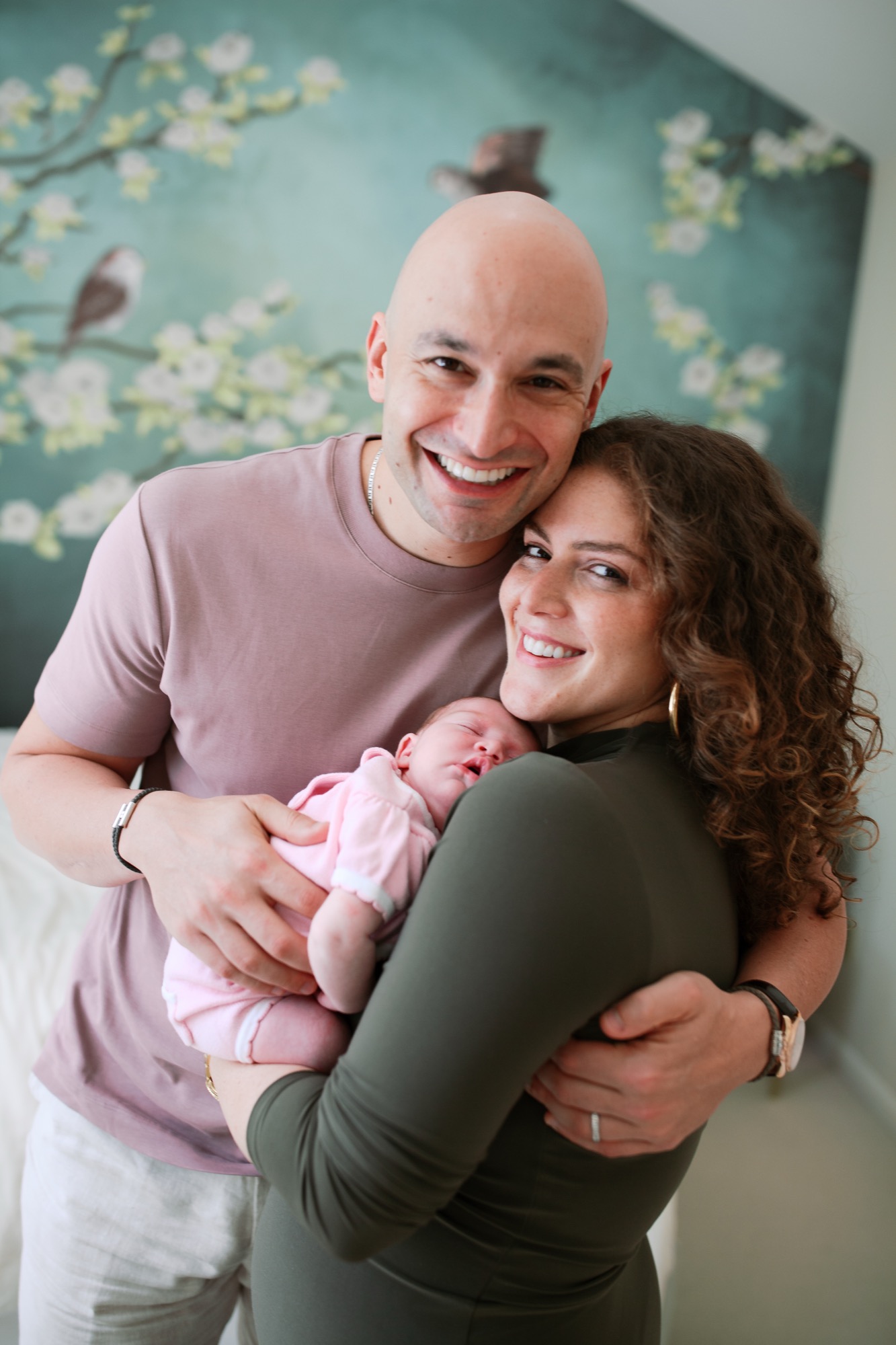 New parents beam with joy as they hold their sleeping newborn in pink against a serene teal floral backdrop