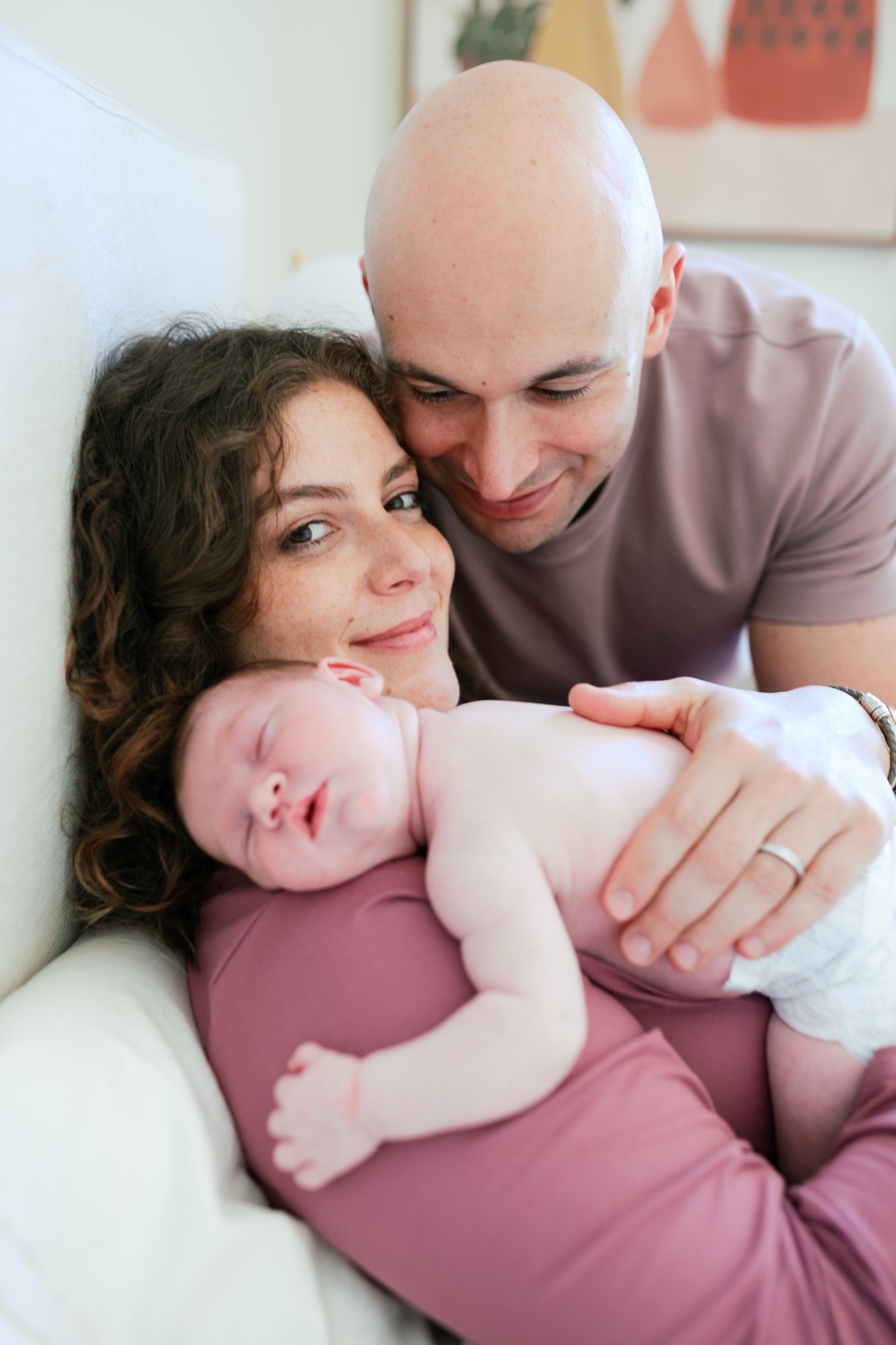 Marin newborn photographer captures a tender family portrait as new parents cradle their sleeping two-week-old in soft, warm light at their Palo Alto home — intimate lifestyle newborn photography in the Bay Area.