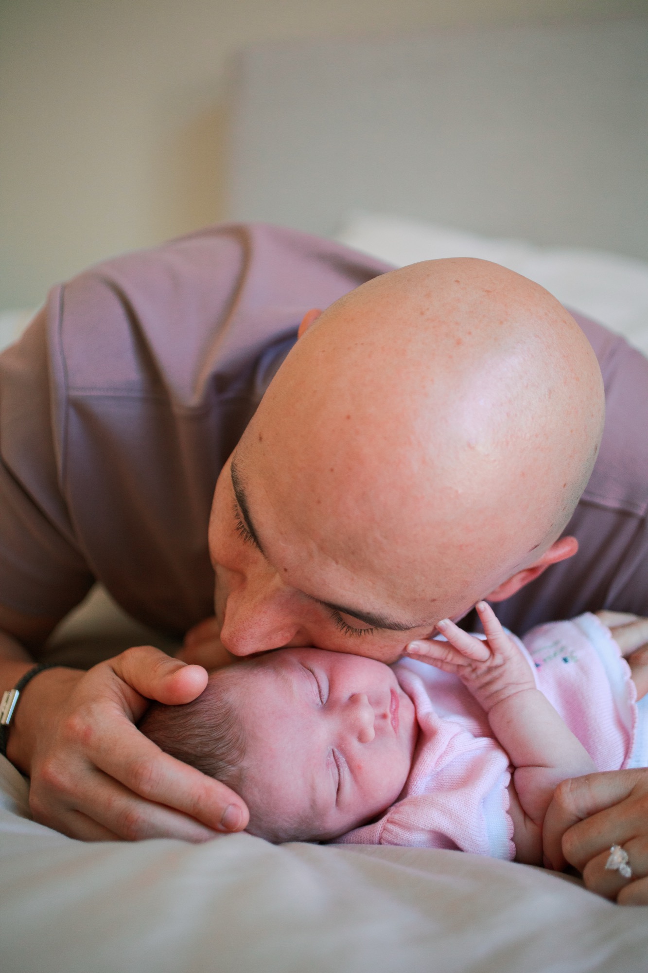 A father tenderly kisses his newborn's forehead, her tiny hand reaching upward in a quiet moment of connection
