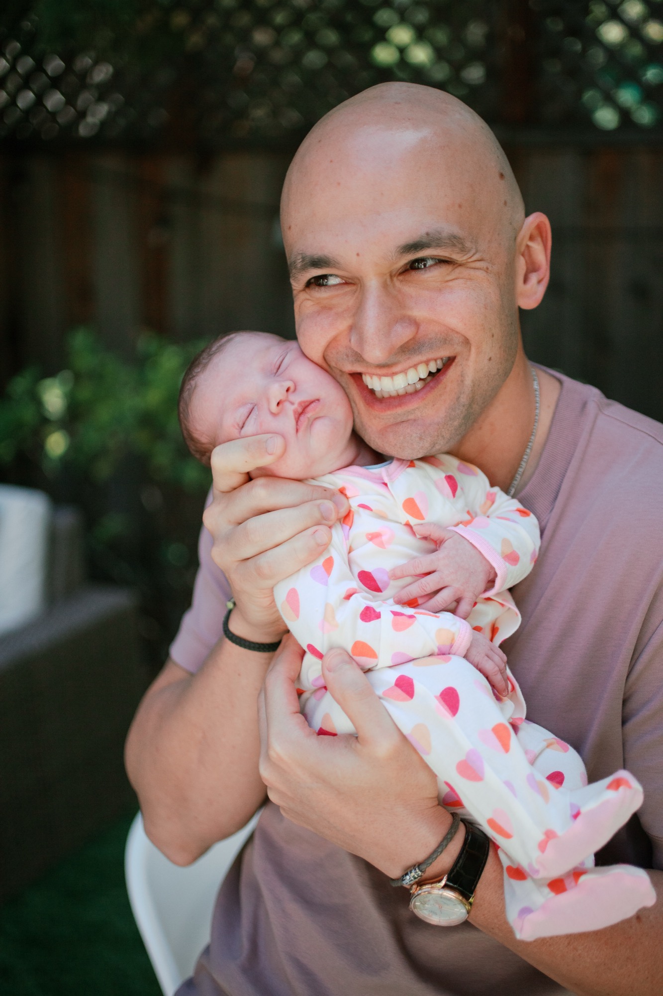 A father holds his newborn against a softly blurred warm backdrop, both at ease in their home