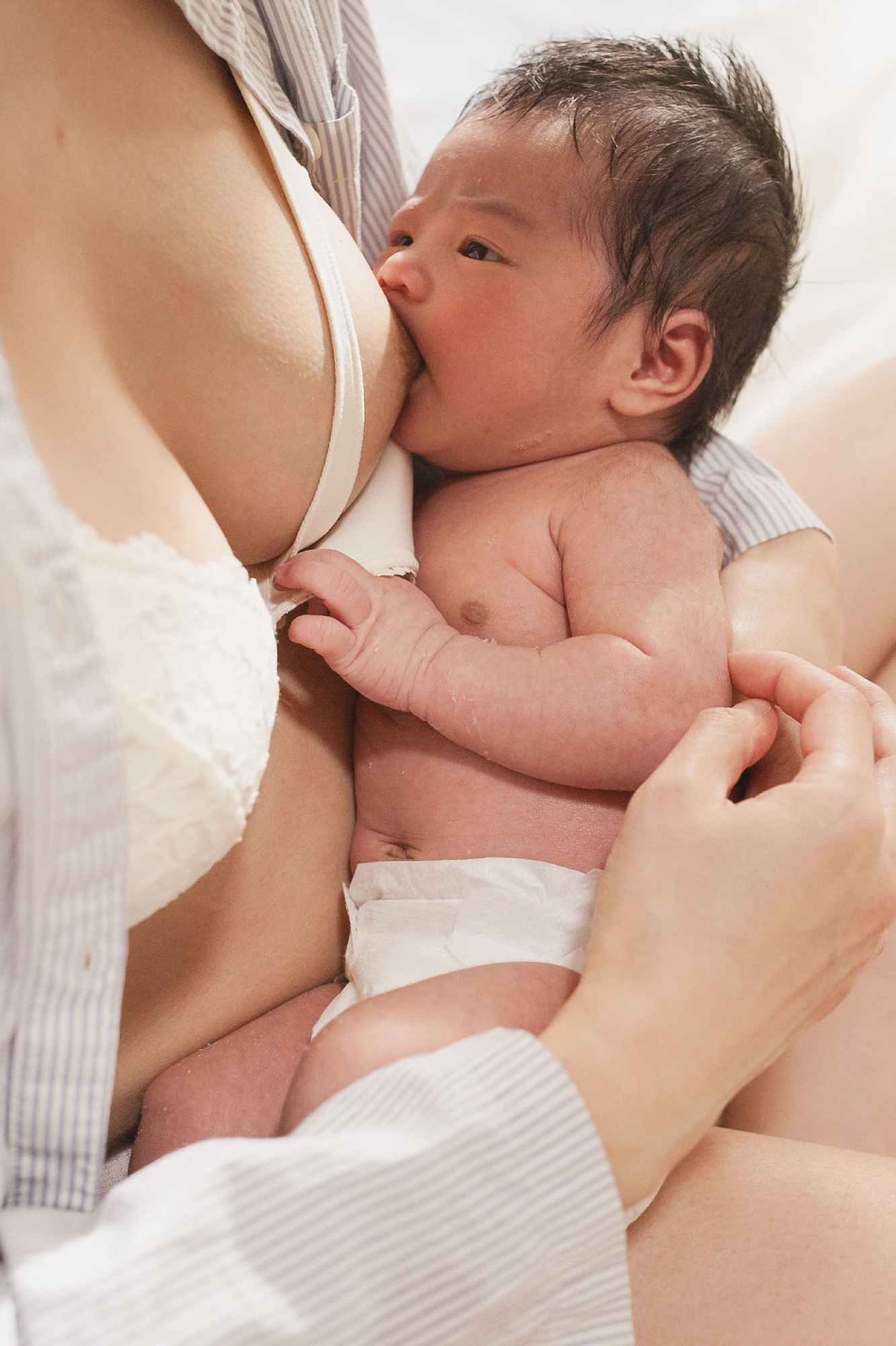 Newborn nursing peacefully against mother's chest while she cradles him in soft natural light