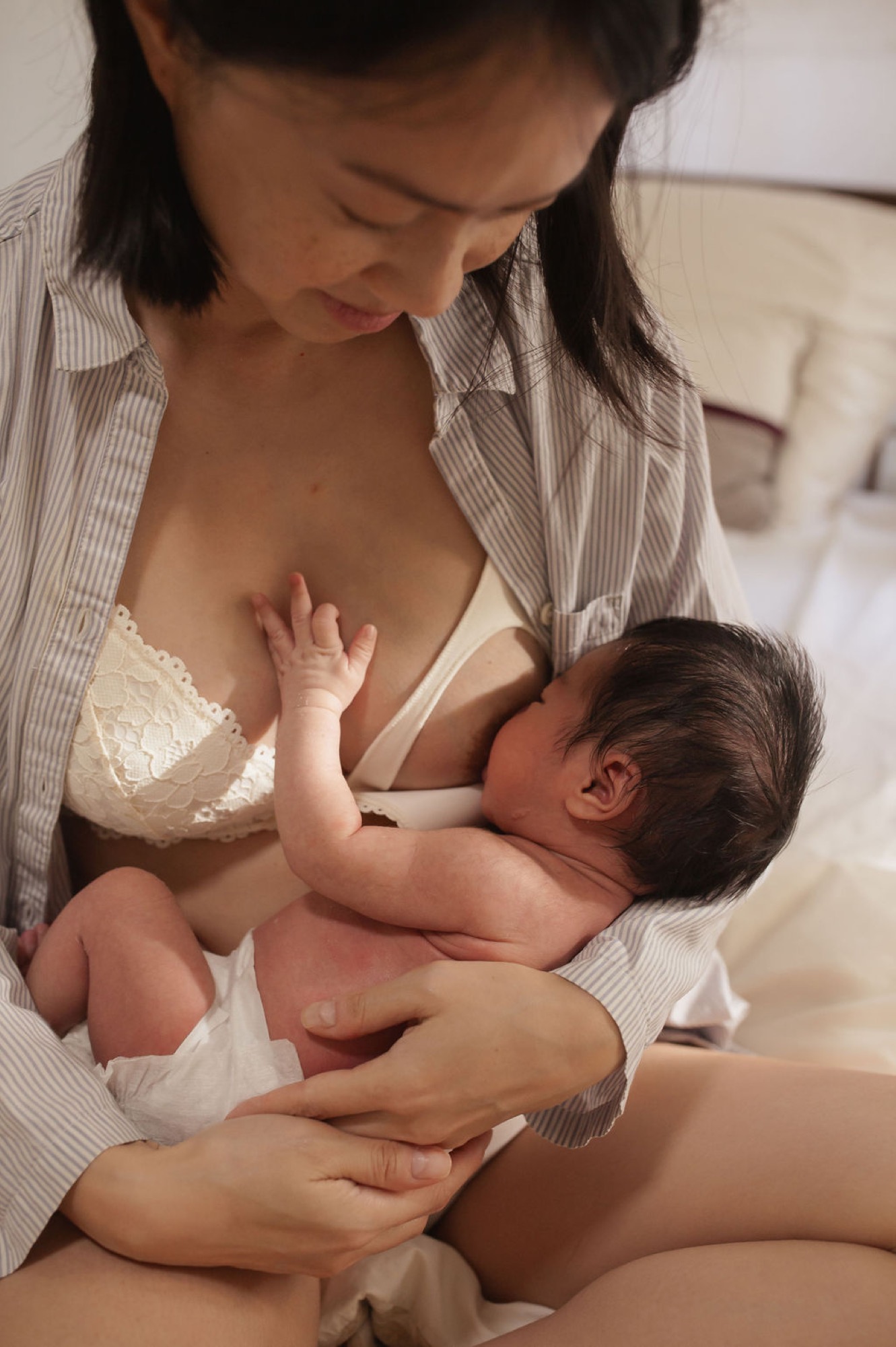 Mother gazes down tenderly at her newborn nursing, her hand gently cradling him in soft indoor light
