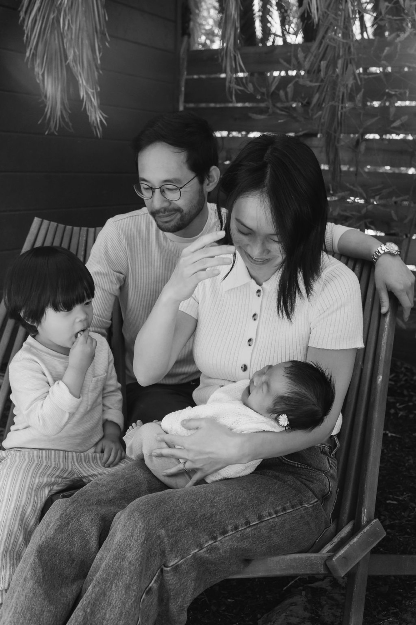 A family of four shares a quiet moment indoors, the newborn cradled in mother's arms while siblings and father lean in with genuine affection and wonder