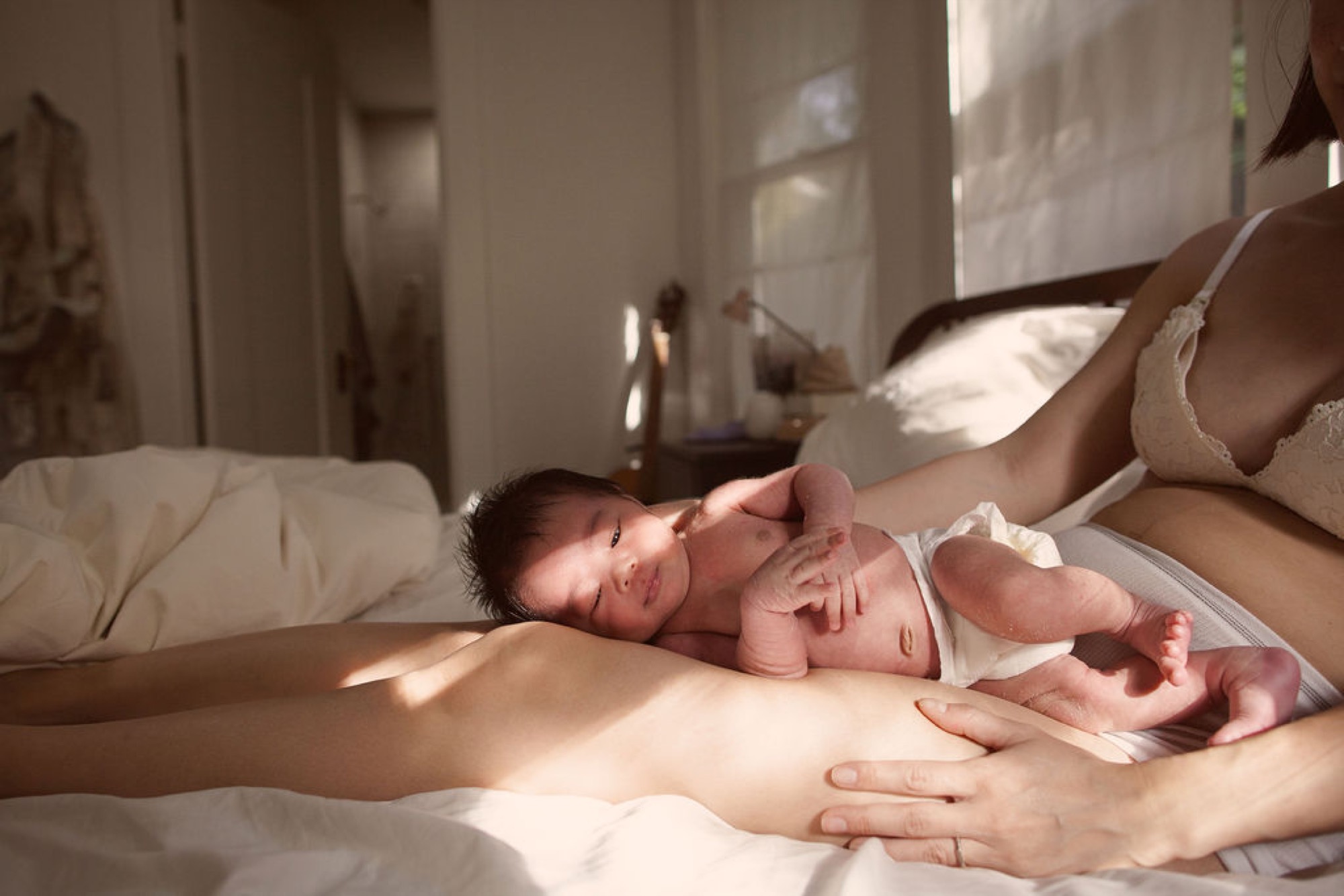 Newborn sleeps peacefully on mother's chest while she gazes down with tender hands cradling the infant in warm natural light