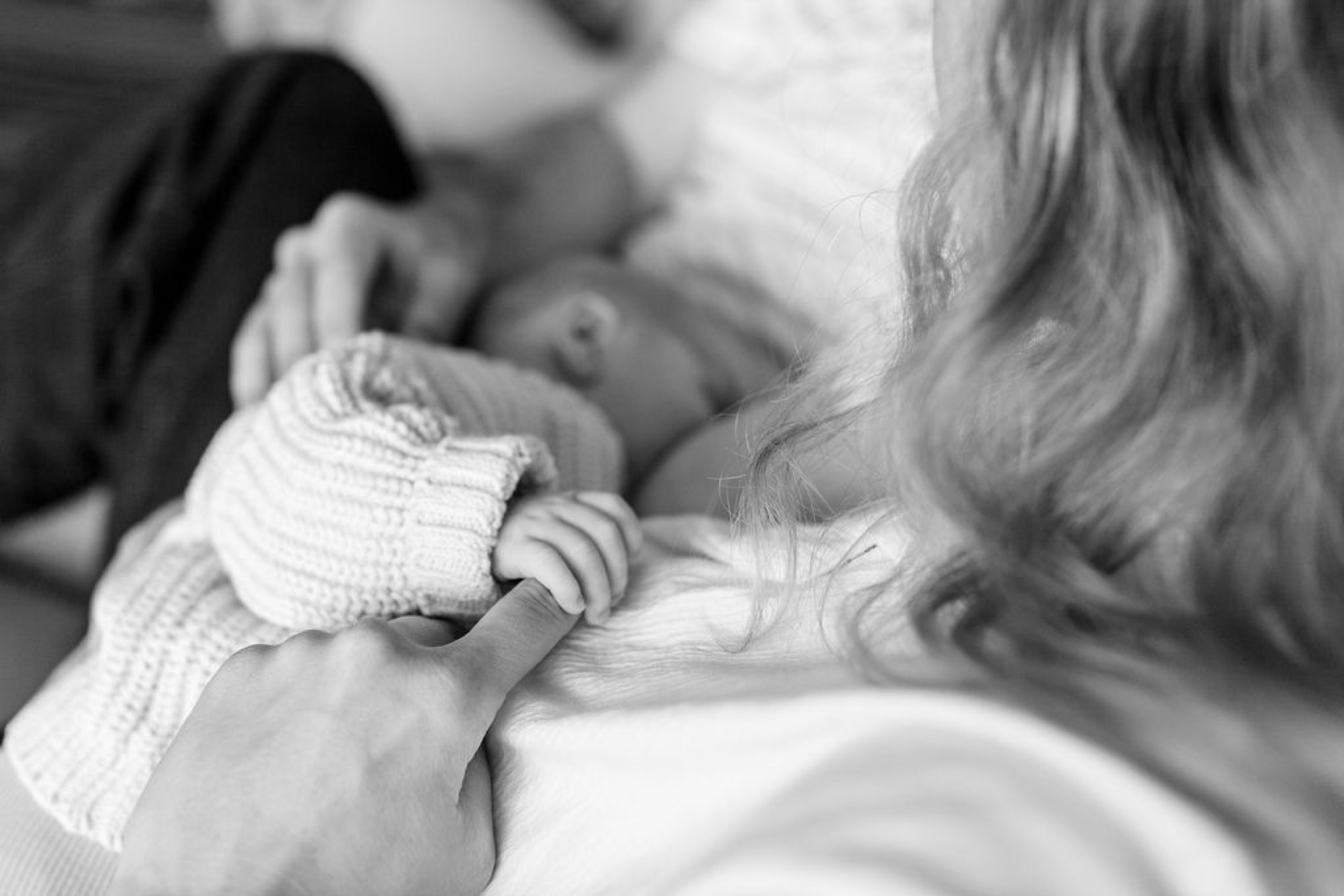 Newborn's delicate hand grasps mother's long hair in black and white, capturing tender intimacy and trust
