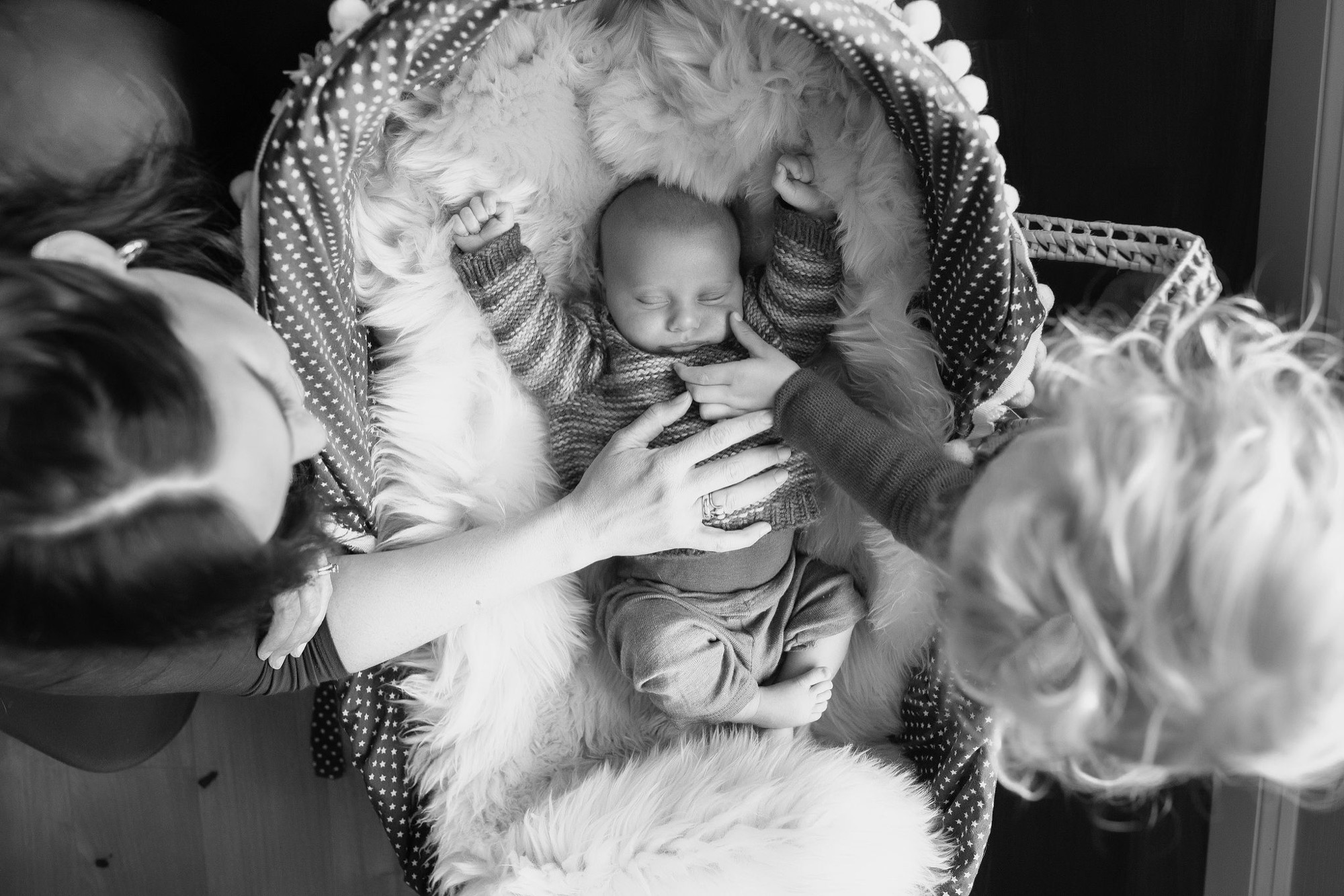 Newborn sleeps peacefully in ornate bassinet surrounded by two older siblings gently touching and admiring their baby brother