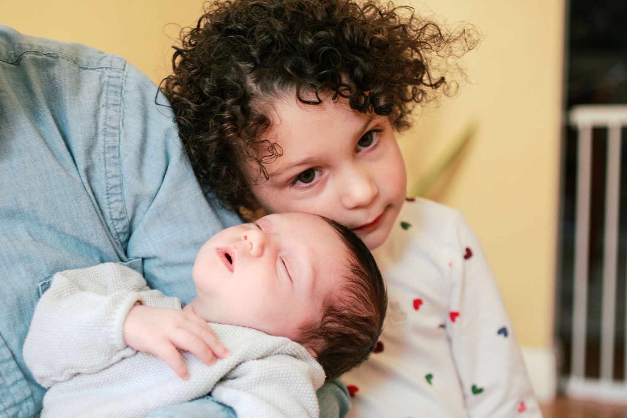 Older sibling gazes tenderly at newborn while cradling them against his chest in soft natural light