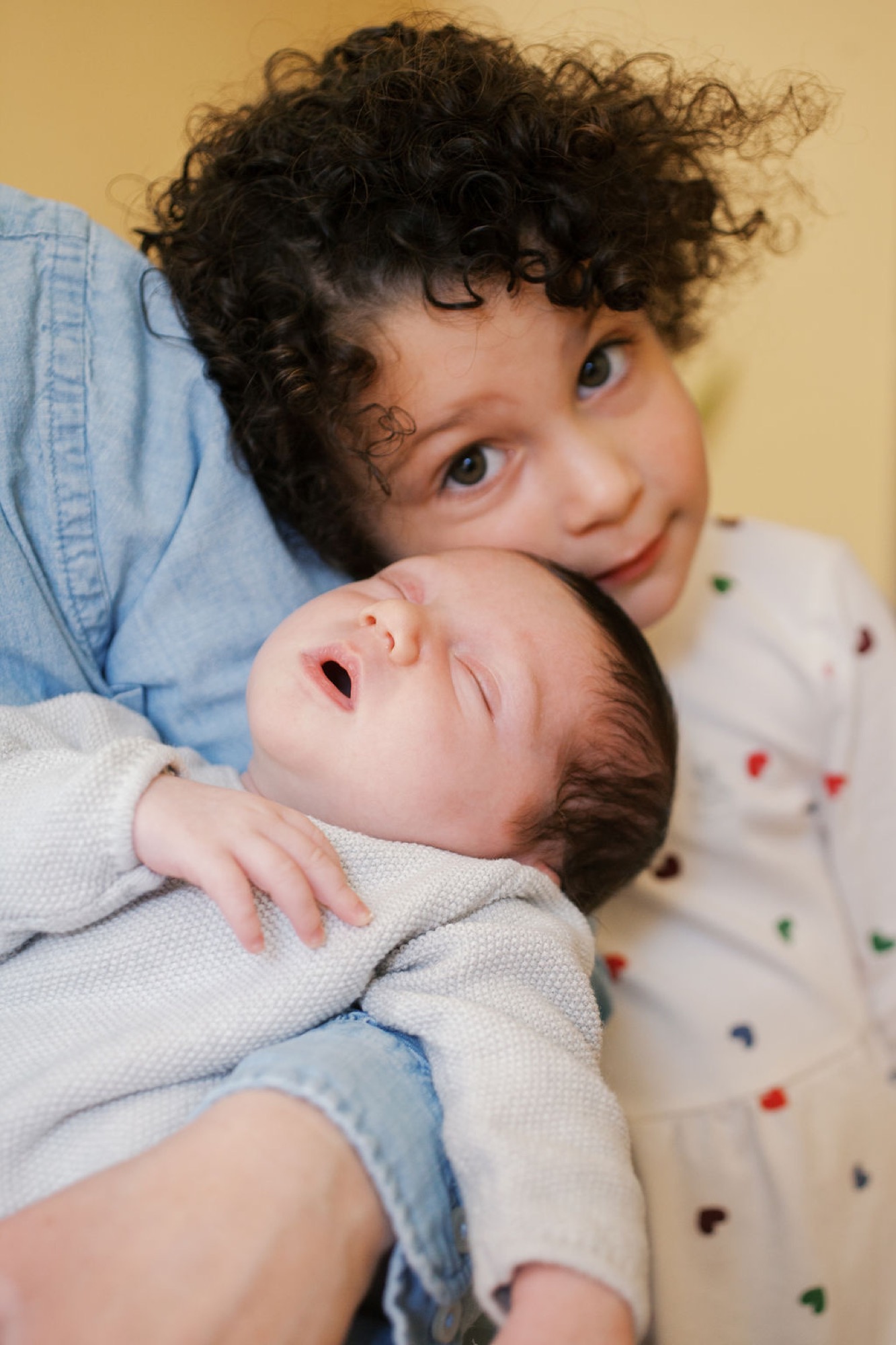 Older sibling gazes warmly at newborn while cradling them against chest in soft natural light